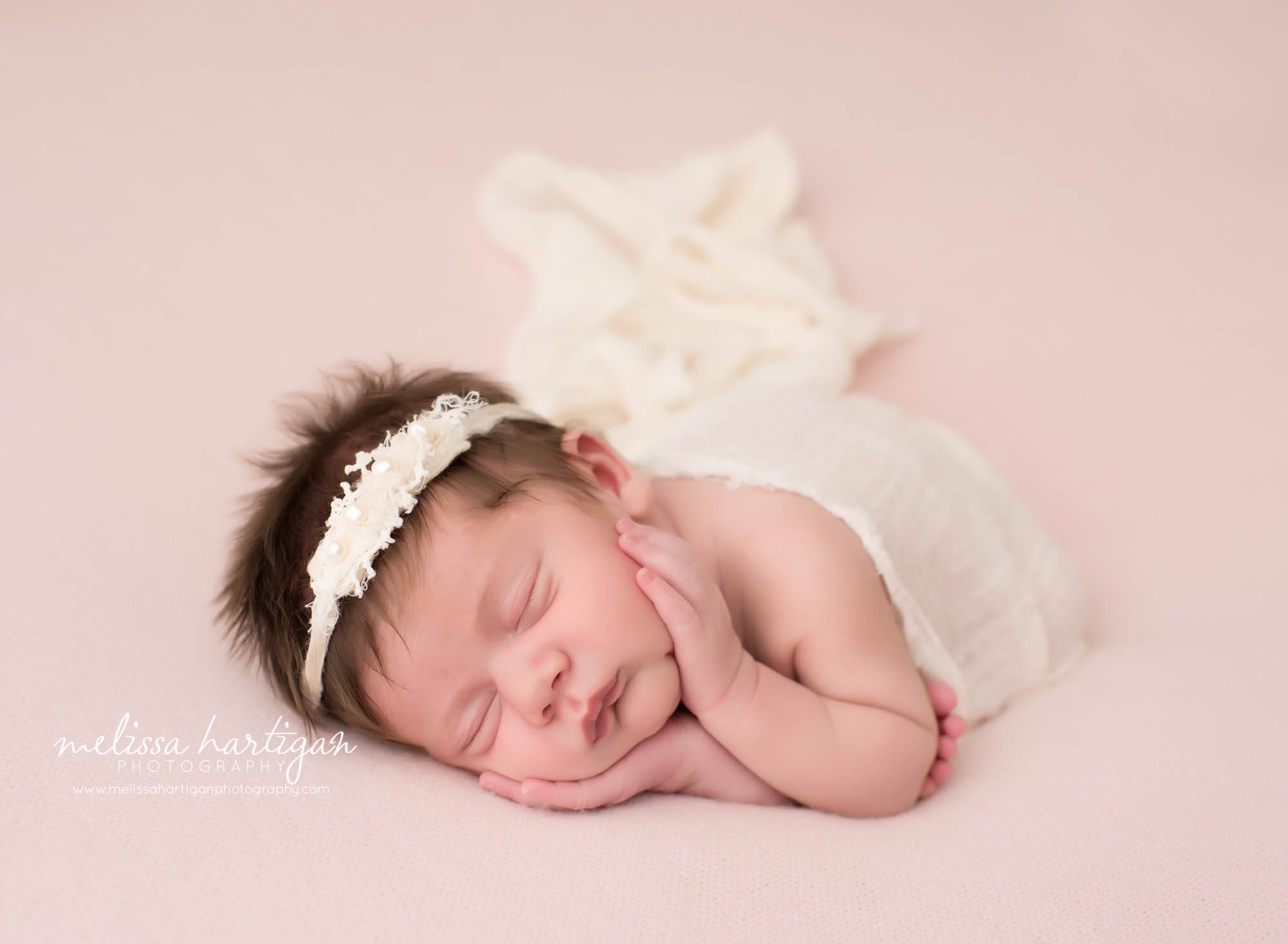newborn baby girl posed timber pose on side holding cheeks wearing cream headband