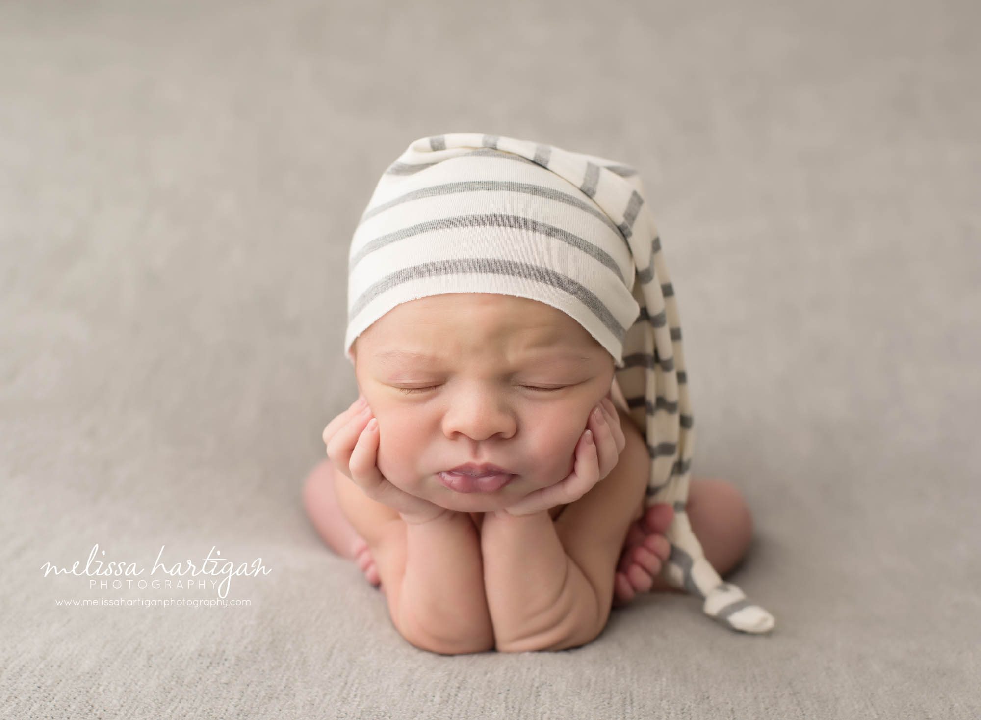 Newborn baby boy posed froggy pose wearing cream and gray striped sleepy cap North Haven CT baby photography