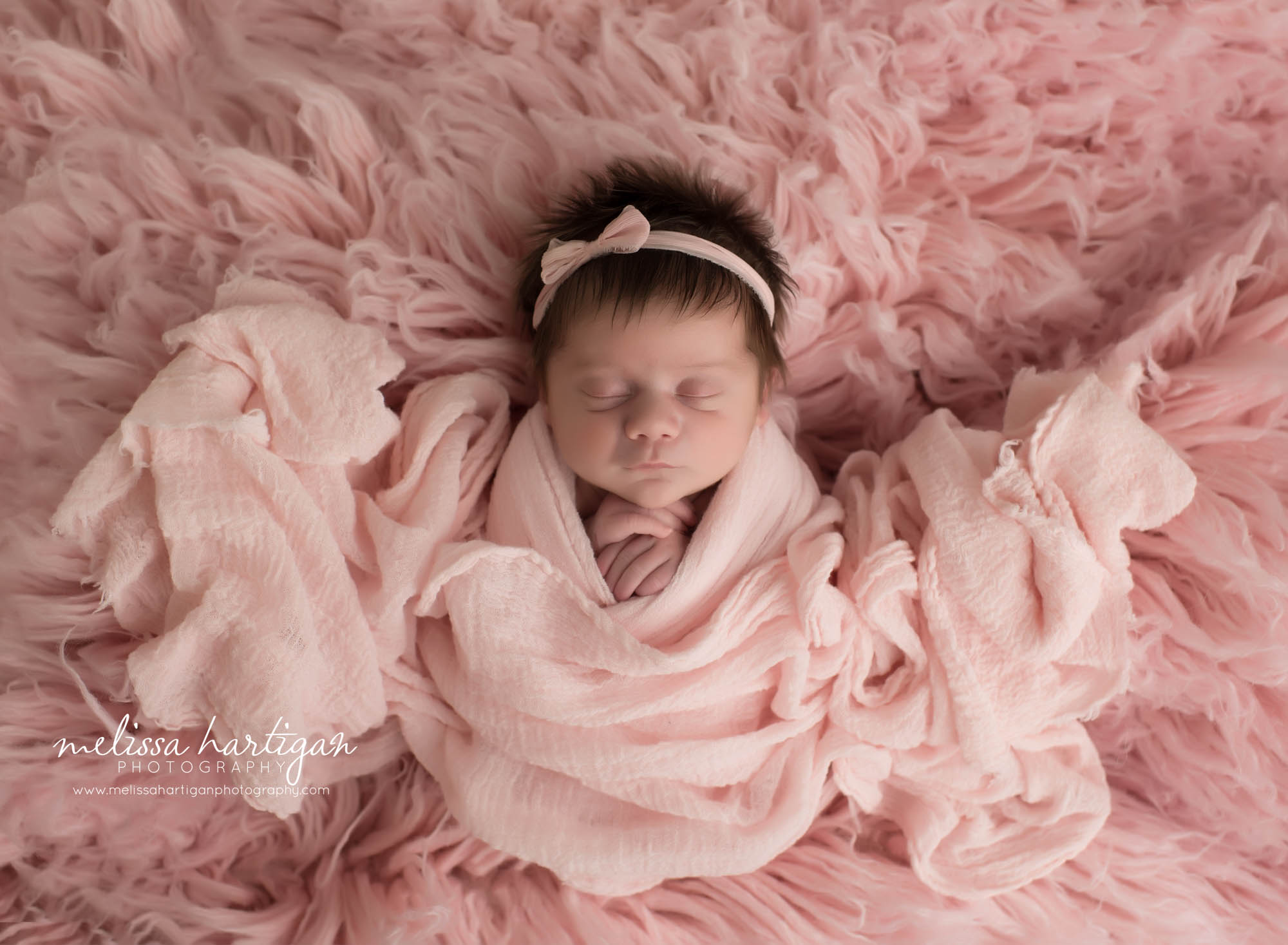newborn baby girl wrapped in pink wrap pose don pink flokati wearing pink bow headband tolland county CT newborn photographer