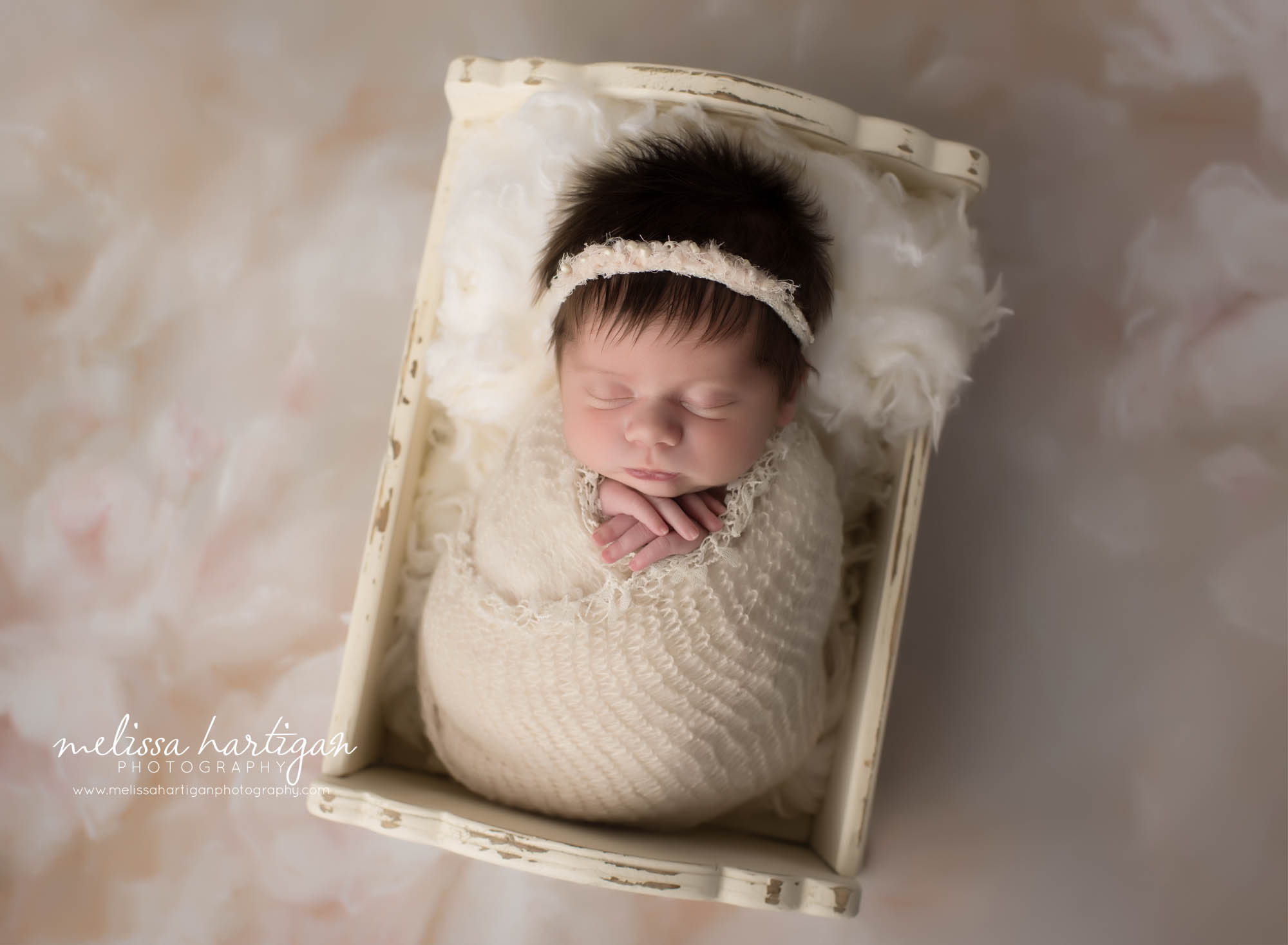 newborn baby girl wrapped in cream wrap posed in wooden cream cradle