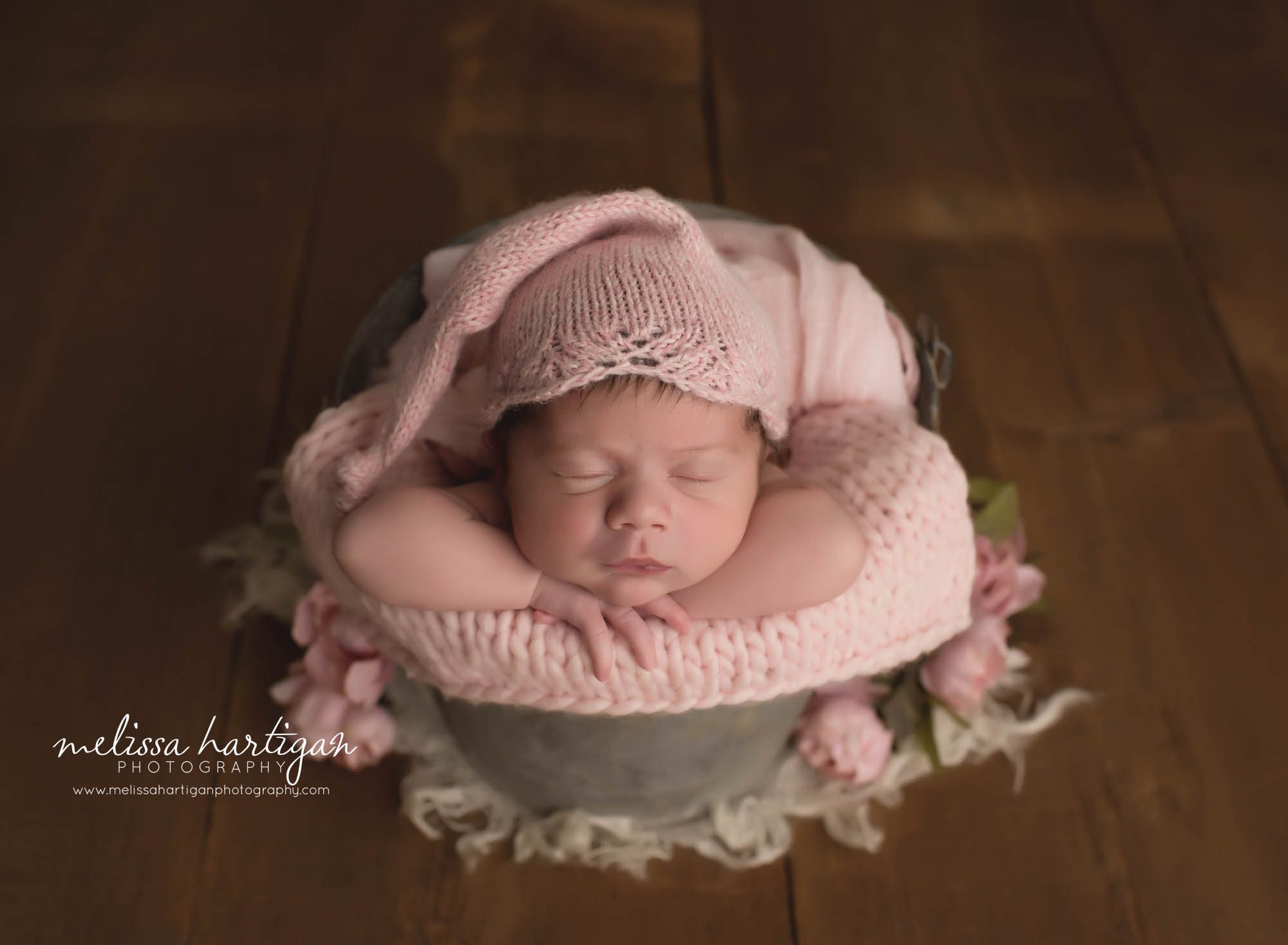 newborn baby girl posed in bucket wearing knitted sleepy cap in light pink rose color