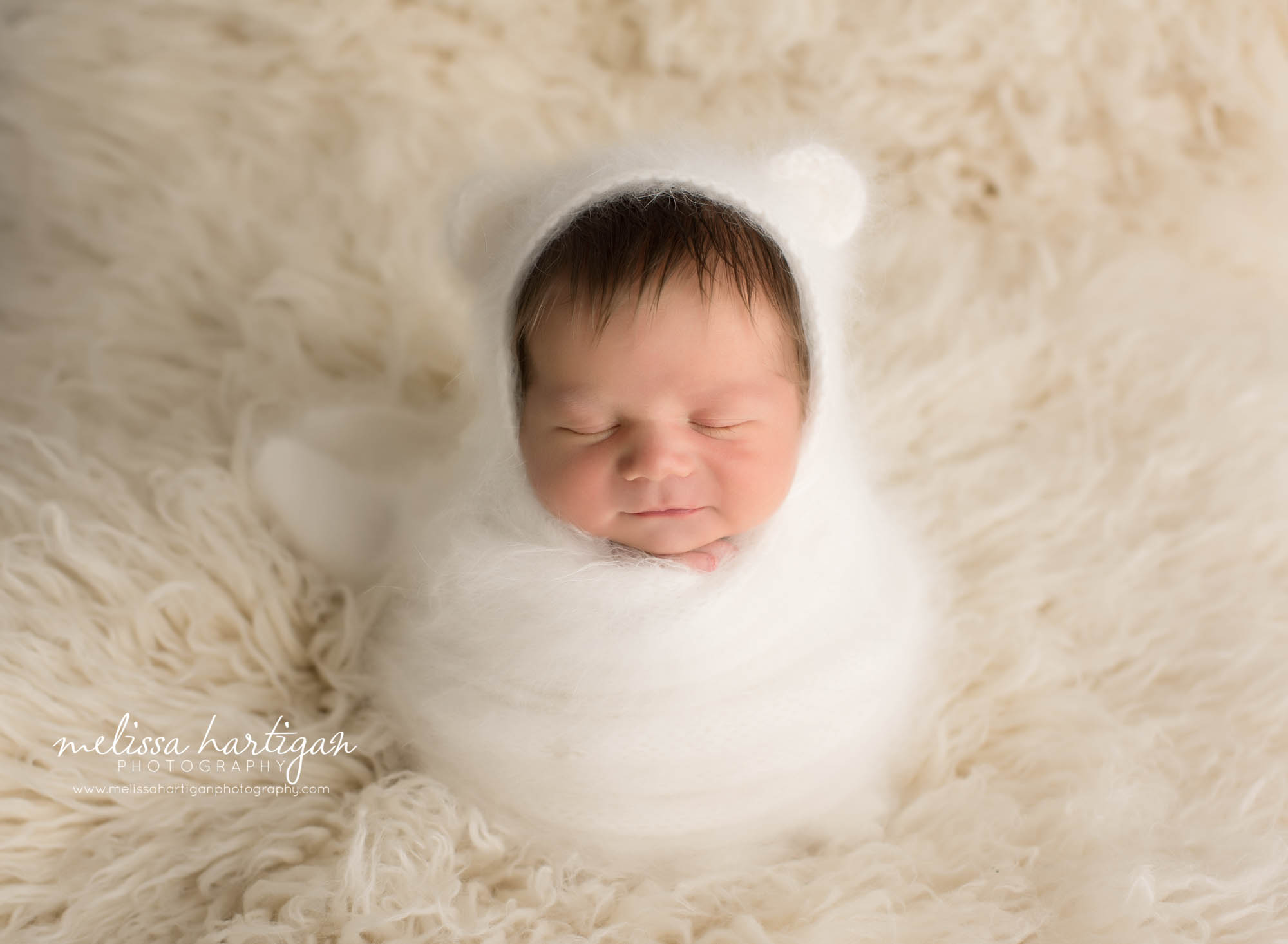newborn baby boy wrapped in cream wrap wearing matching bear bonnet