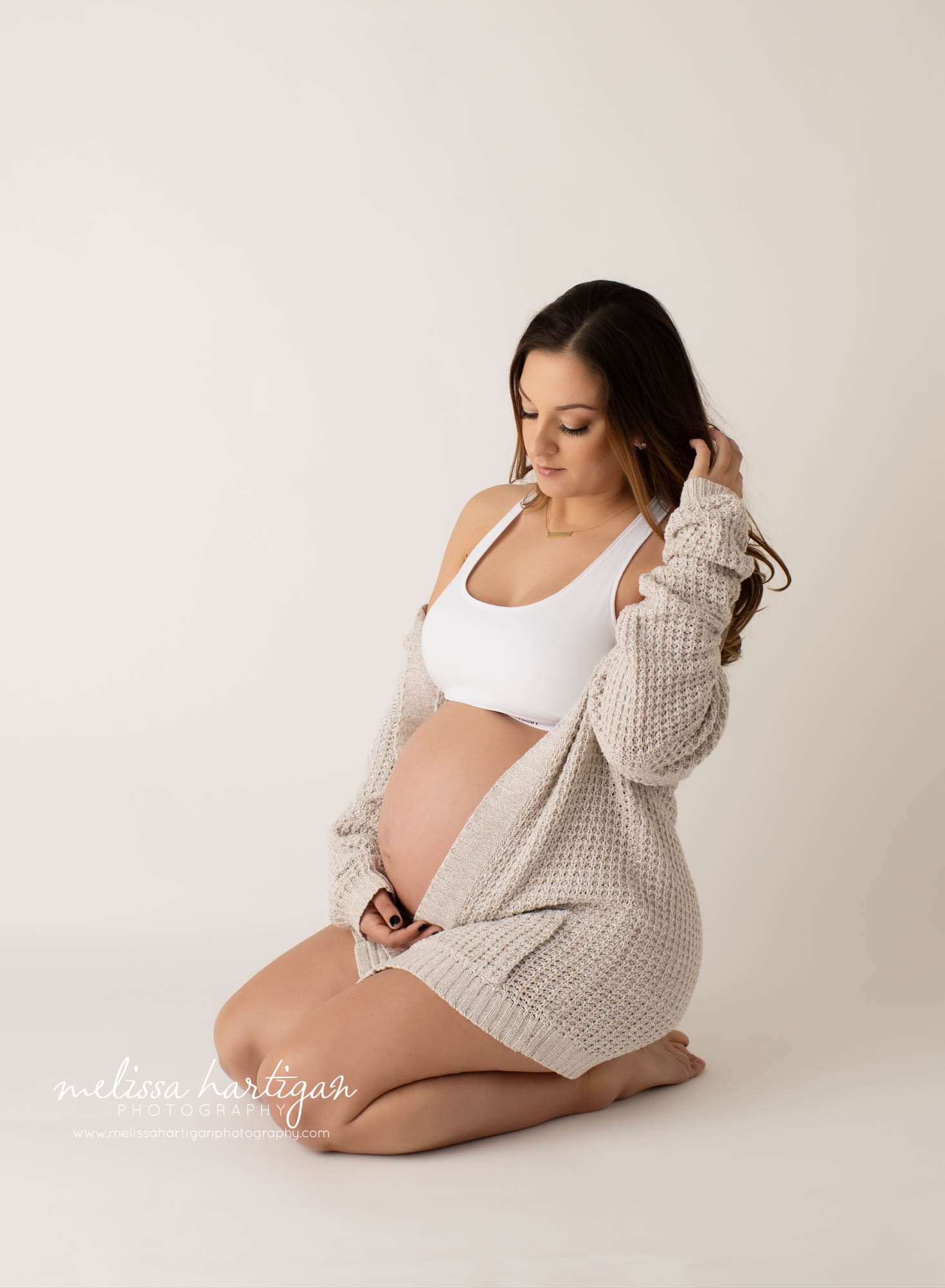expectant mom sitting on floo holding top of baby belly brushing fingers through hair looking at camera hartford county maternity photography