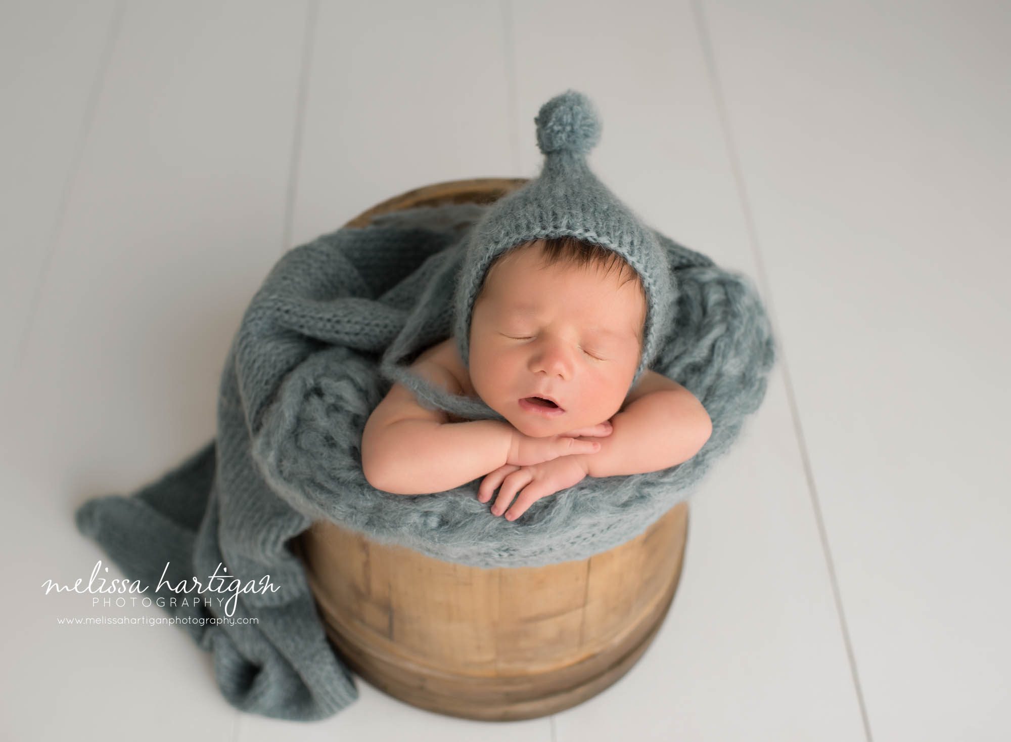 newborn baby boy posed in wooden barrel wearing pom sleepy cap