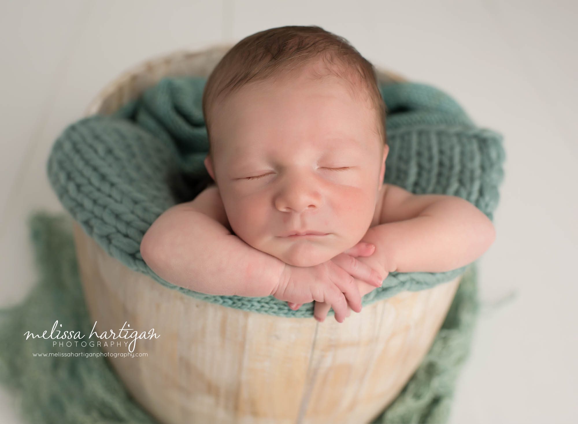 newborn baby boy posed in wooden bucket with treal green knitted layer blanket newborn photography middlesex county photography