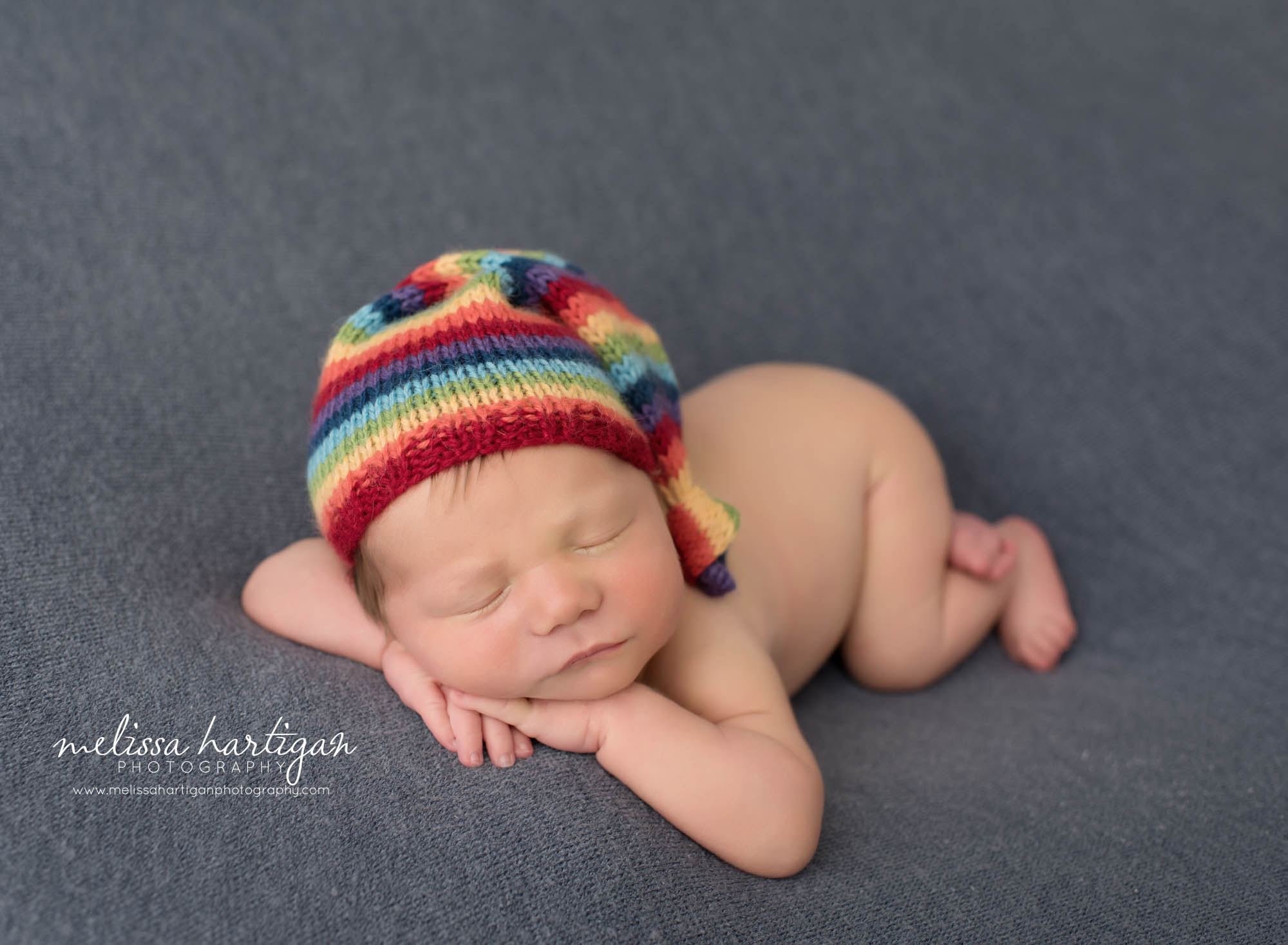 newborn baby boy posed on blue backdrop with rainbow sleepy cap Glastonbury CT newborn photography