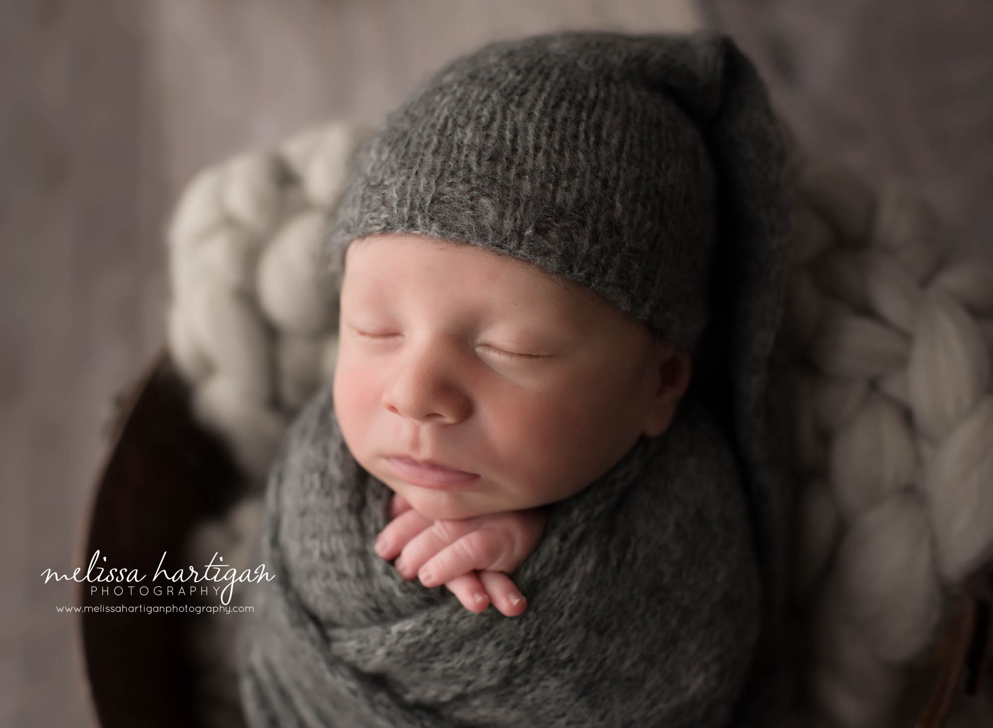 newborn baby boy wrapped in dark gray knitted wrap with matching sleepy cap
