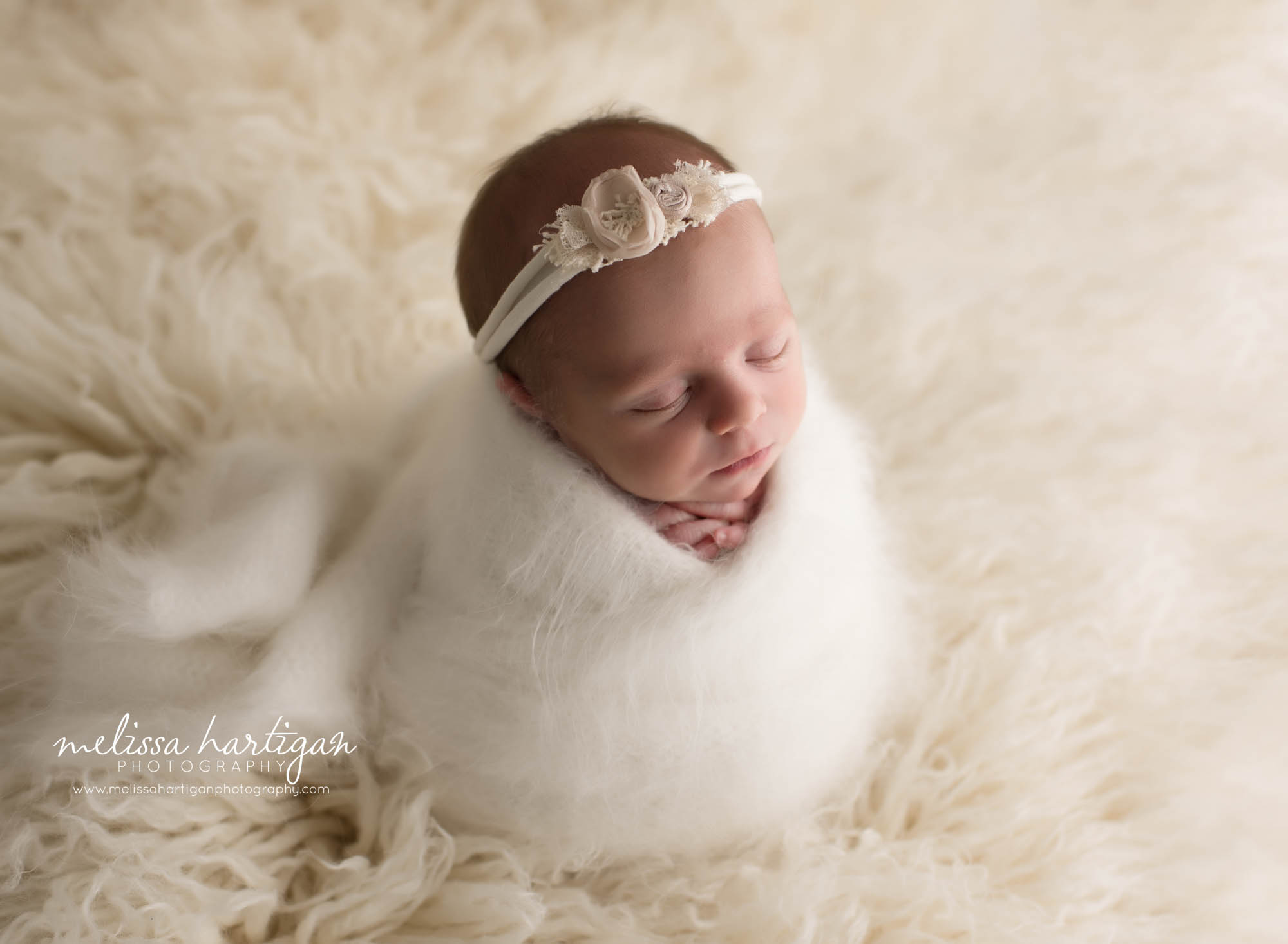 newborn baby girl wrapped in cream wrap posed on cream flokati rug wearing flower headband CT newborn photographers