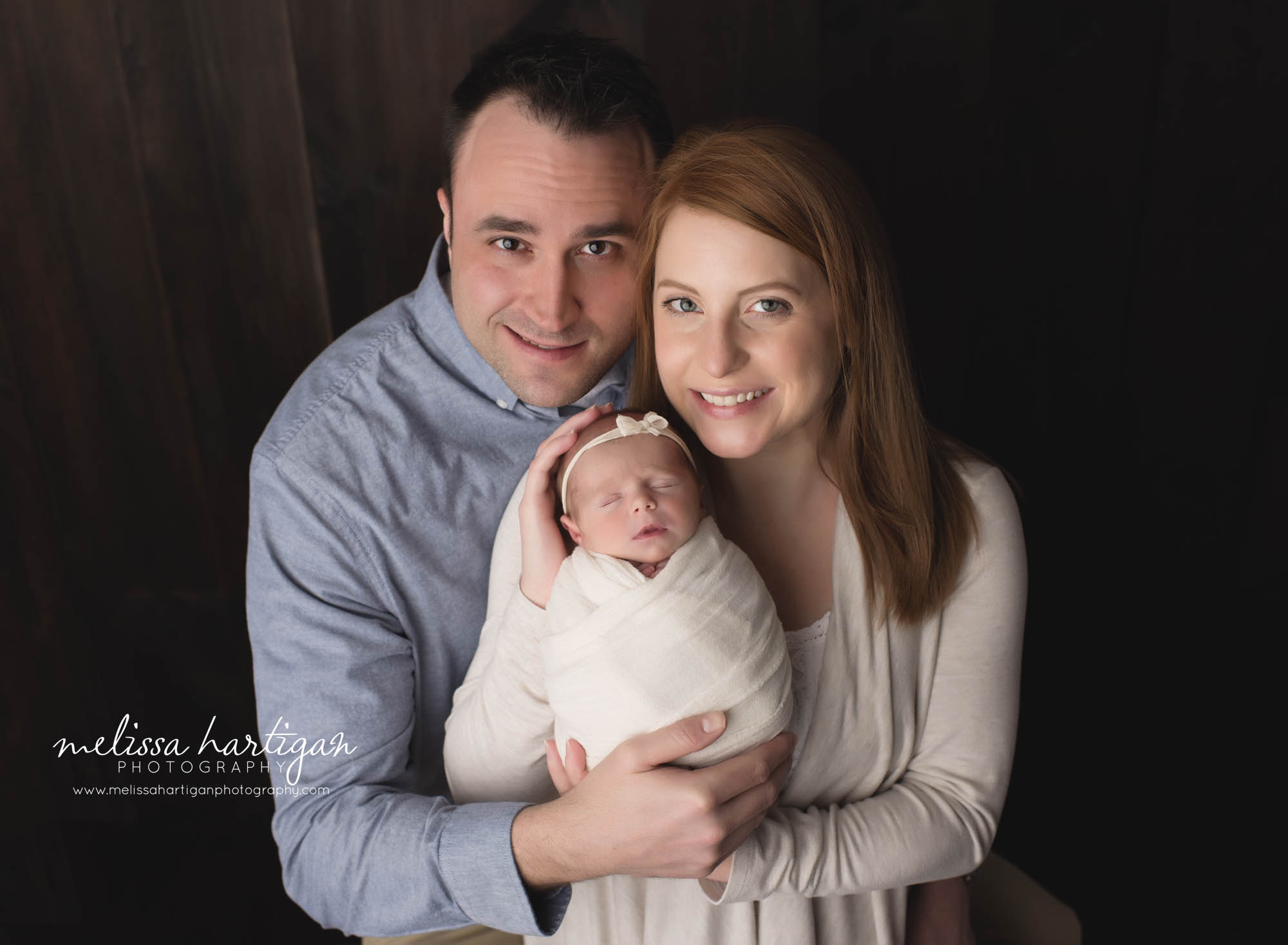 mom and dad holding their newborn baby girl wrapped in cream wrap wearing cream bow studio newborn family photography CT