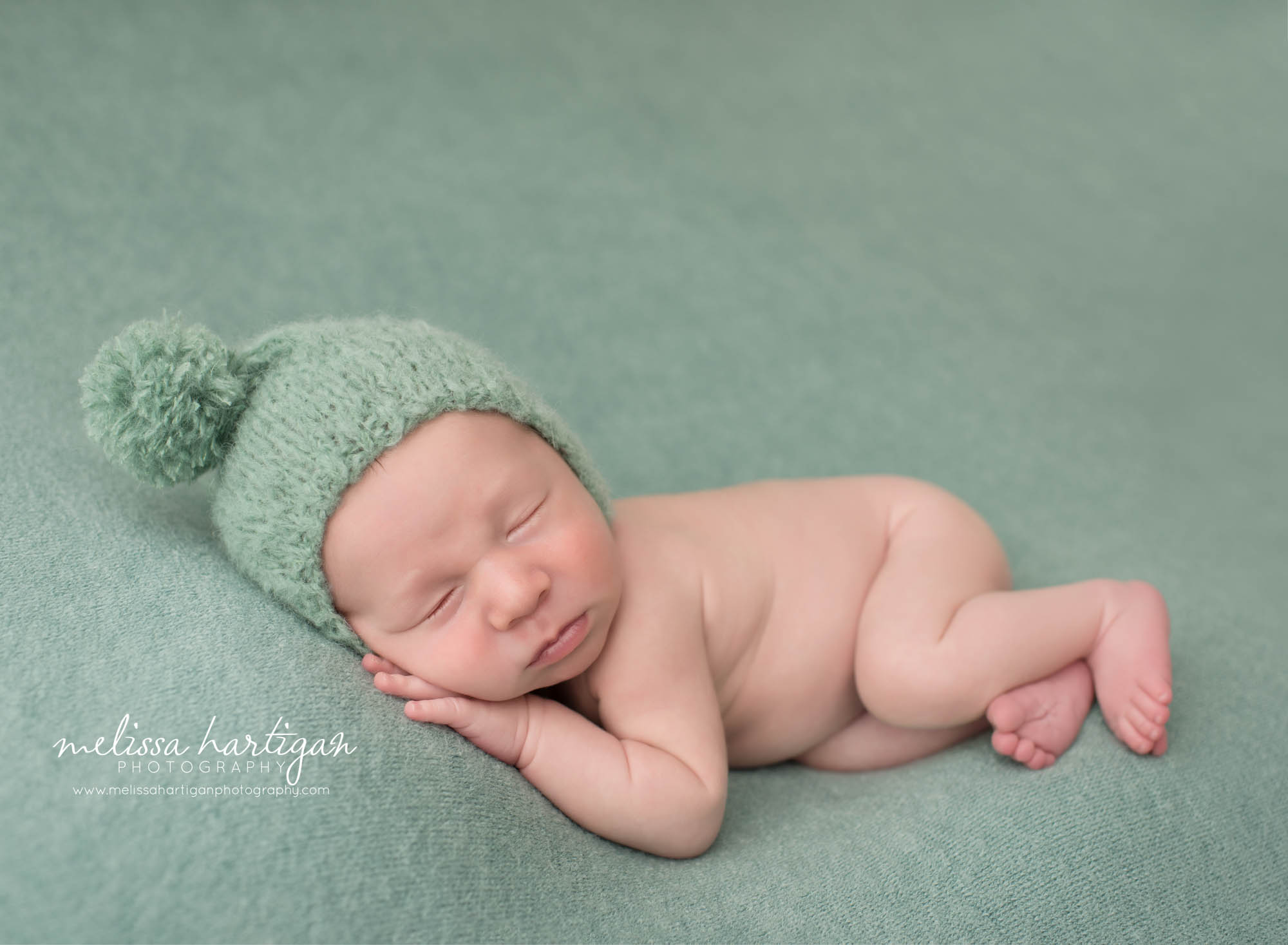 newborn baby boy posed on side with teal green sleepy cap with with pom