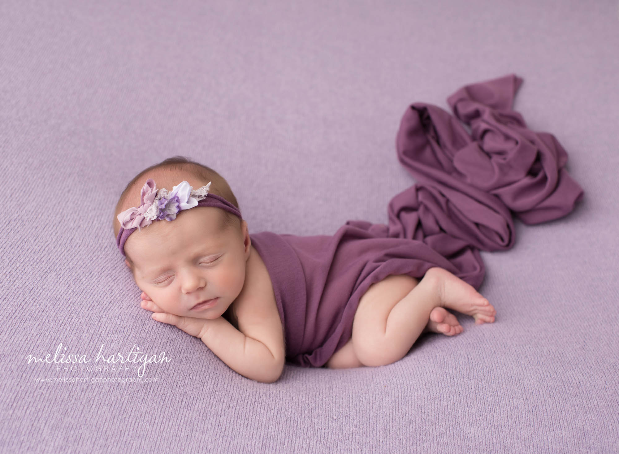 newborn baby girl posed on purple backdrop with dark purple toned layer wrap draped over newborn photography CT