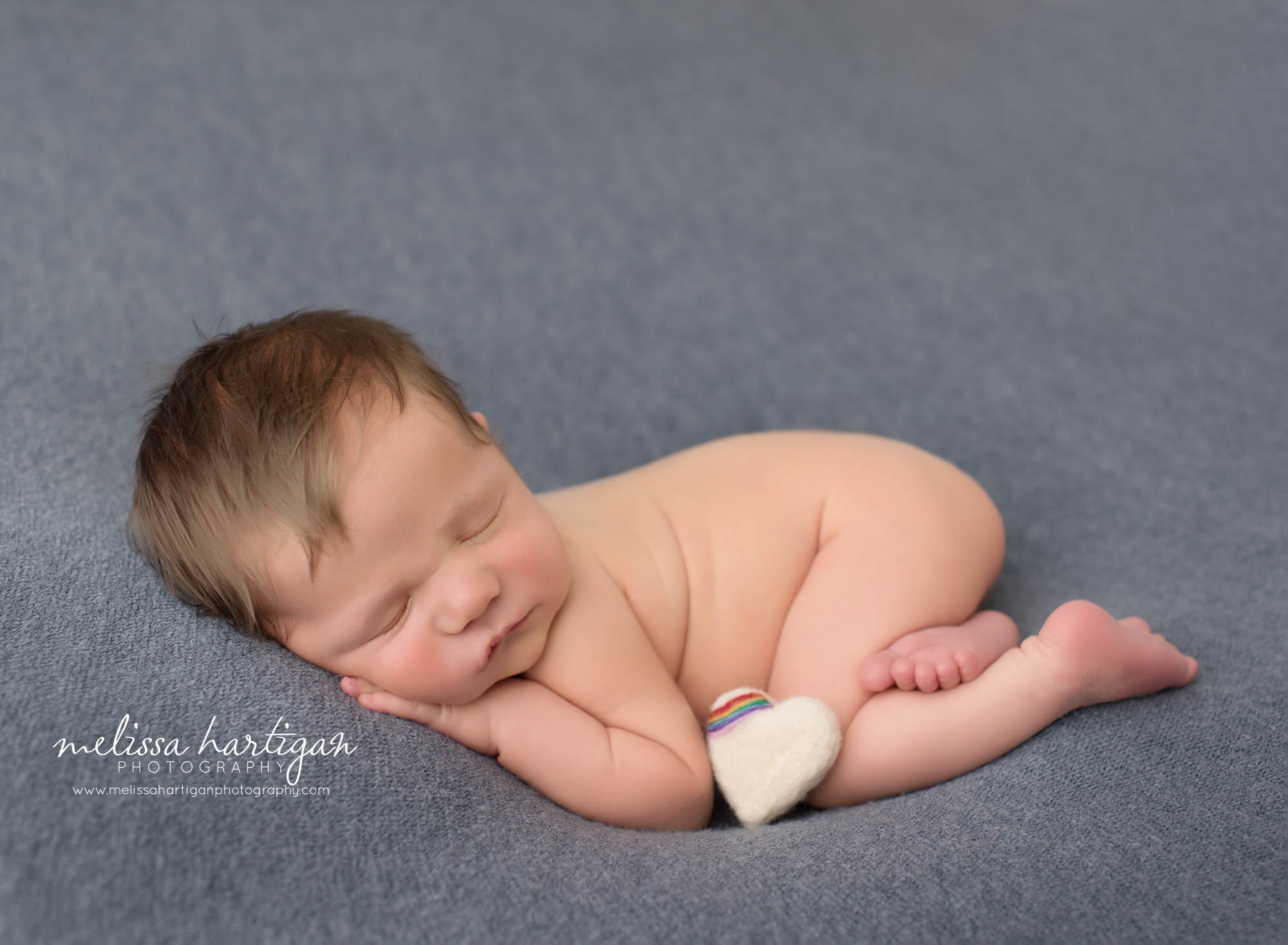 newborn baby boy posed on tummy with white felted heart with rainbow