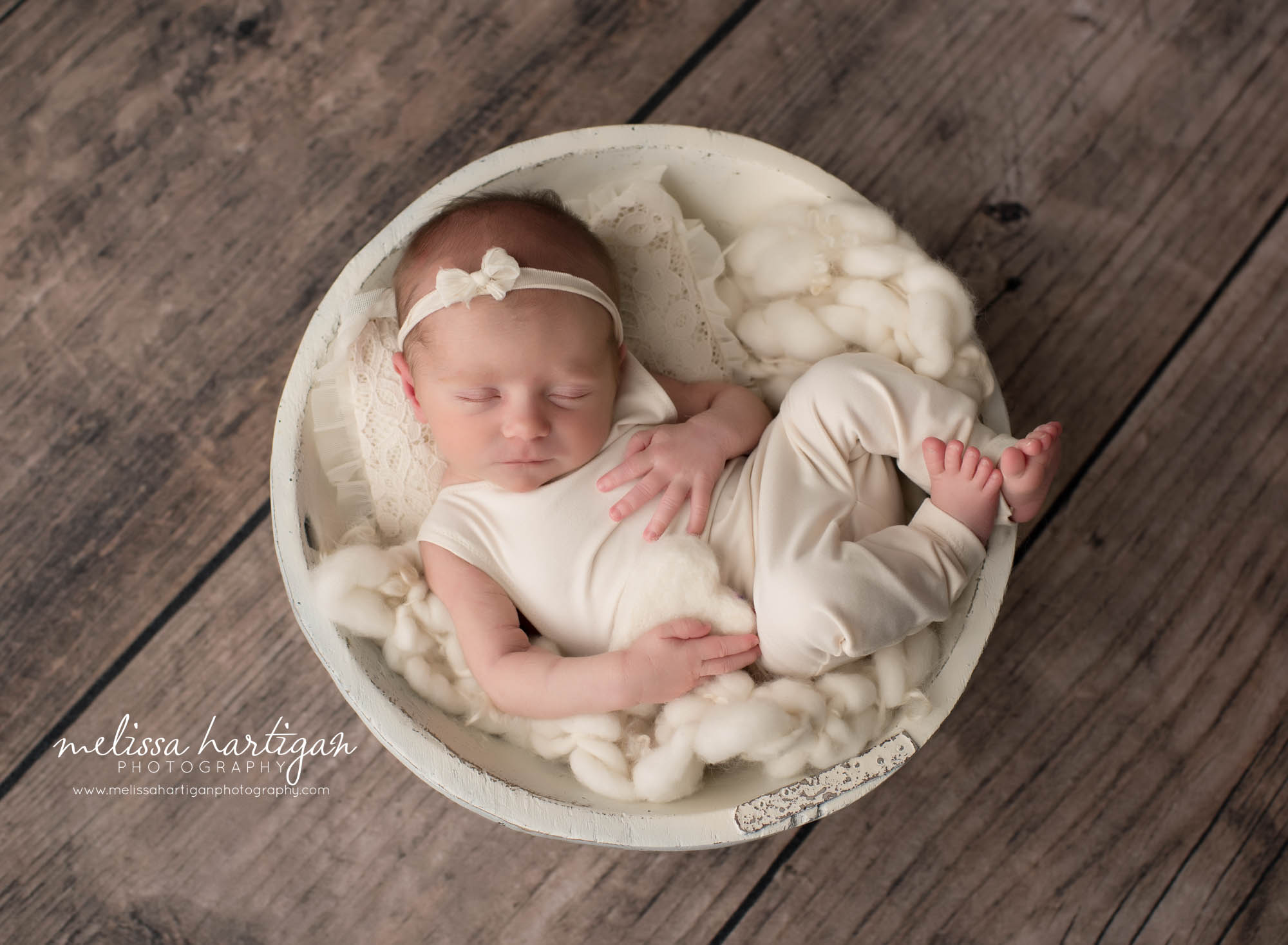 newborn baby girl wearing cream outfit posed in cream wooden bowl with cream layering