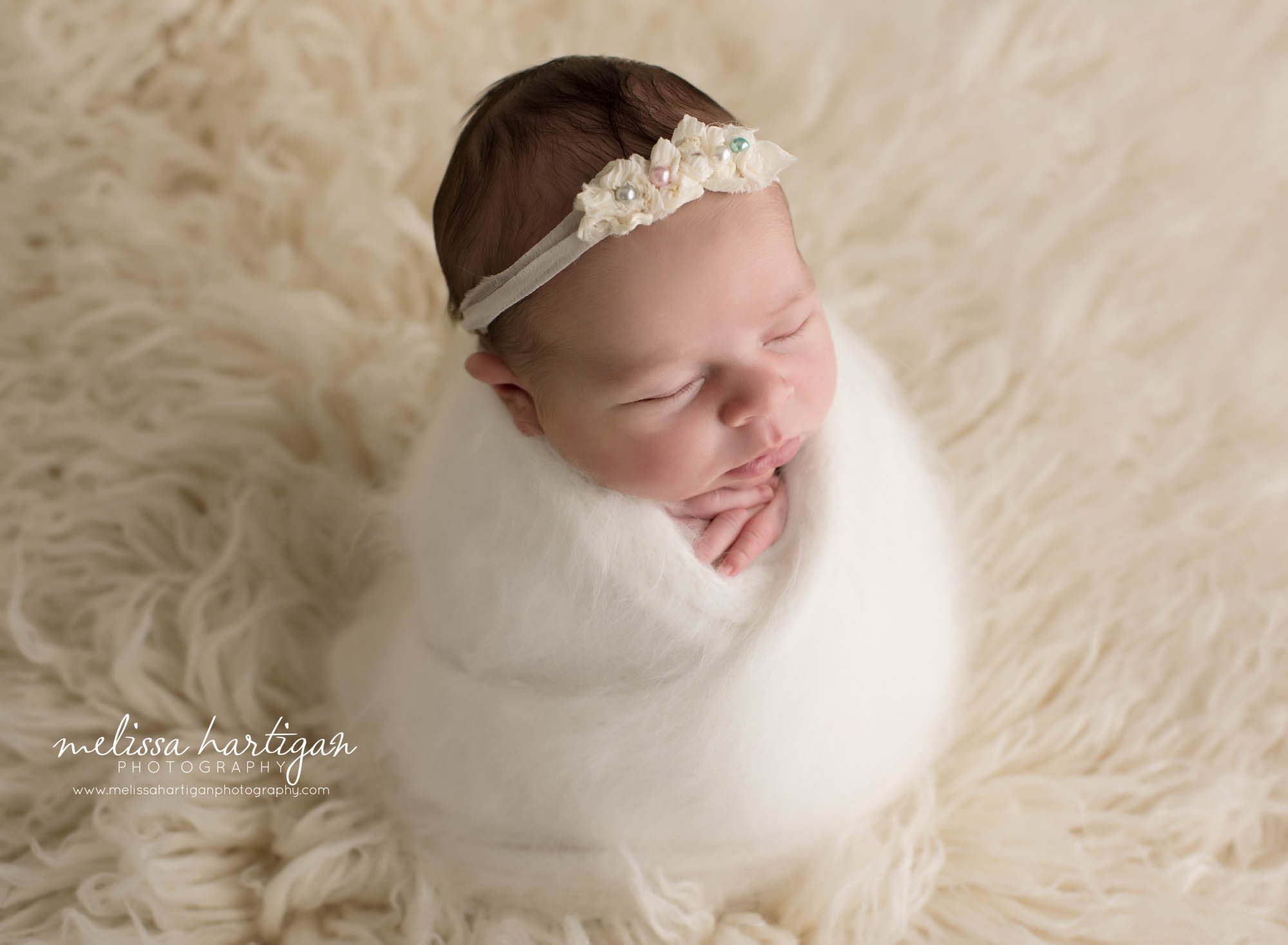 newborn baby girl wrapped in cream wrap with pearl headband