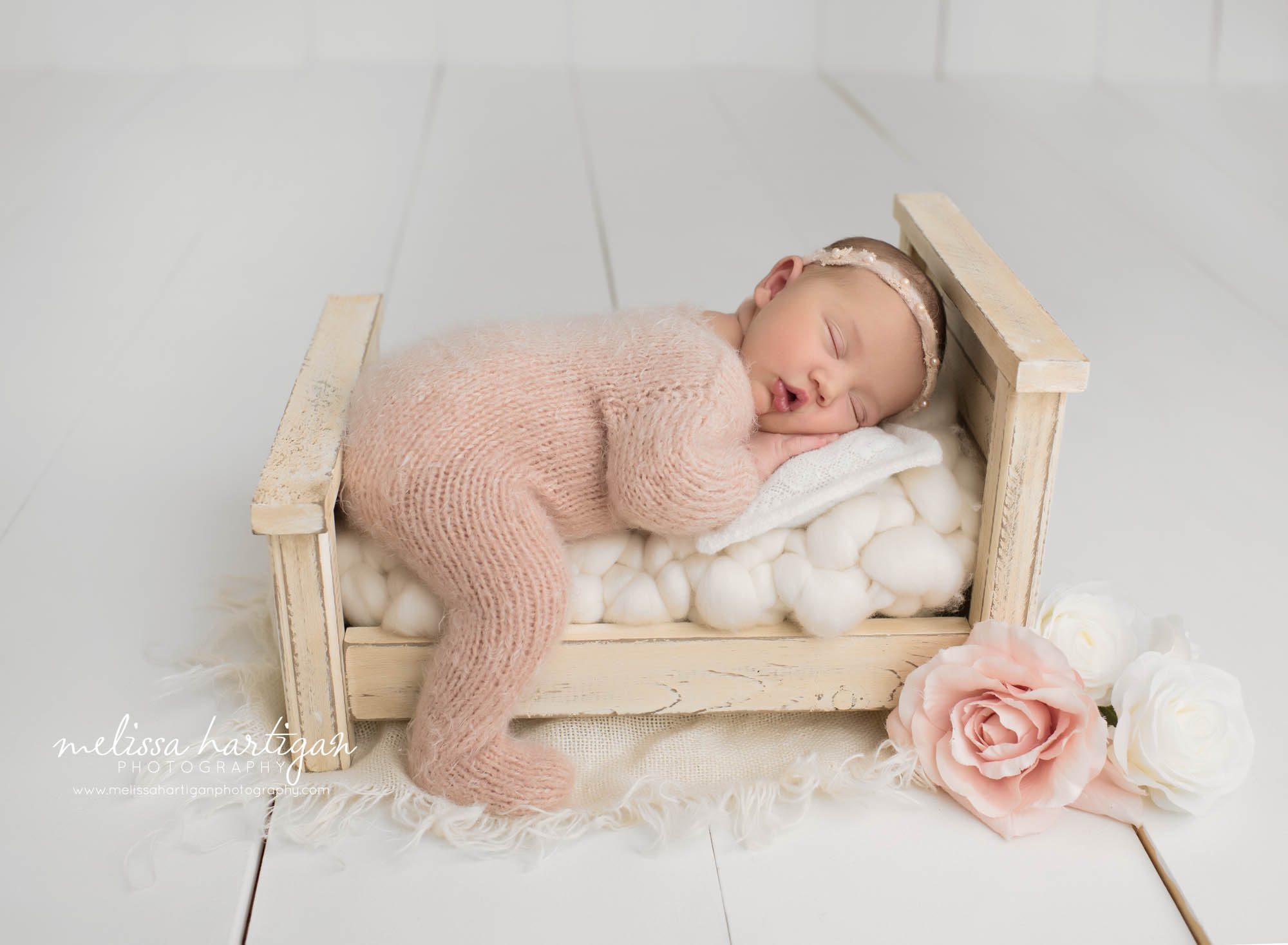 baby girl posed on tummy on wooden newborn prop bed wearing light pink knitted footed sleeper