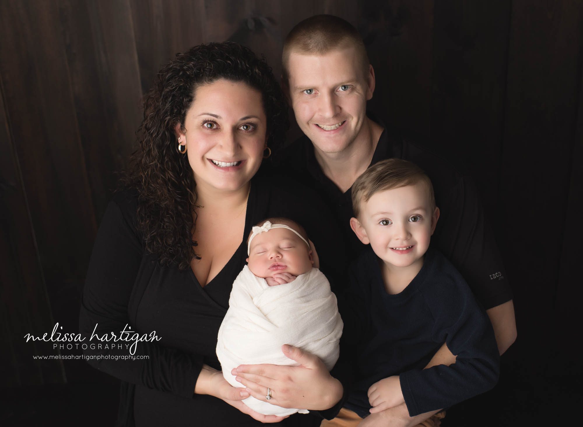mom dad big brother and newborn baby girl wrapped in cream wrap posed together for family pose CT baby photography