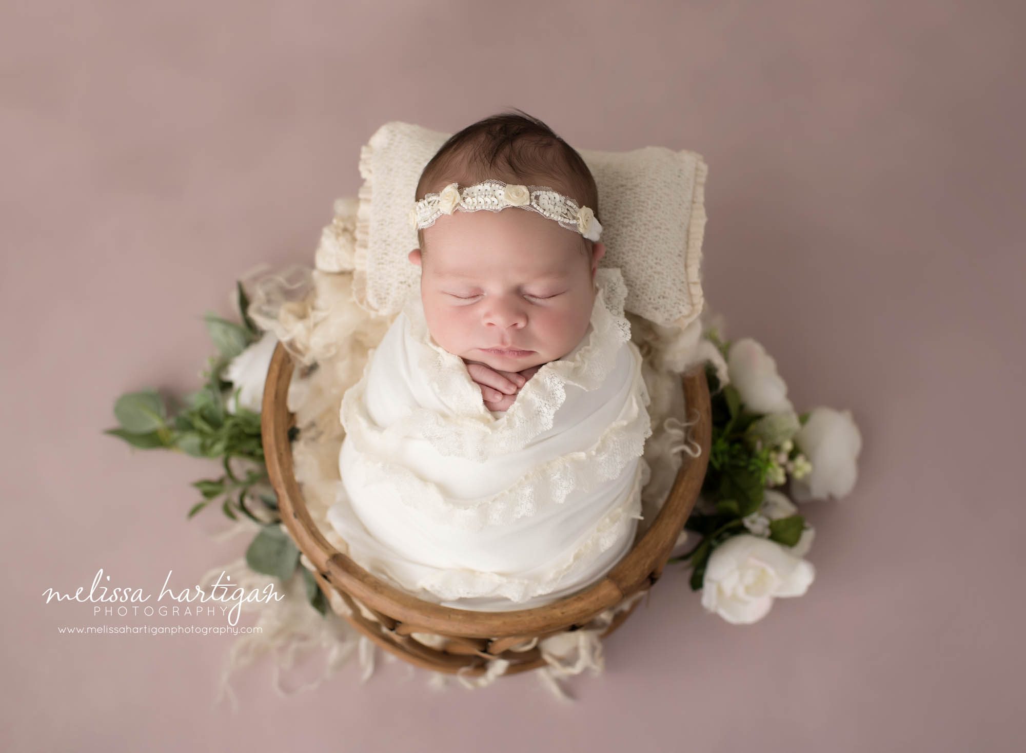newborn baby girl wrapped in cream wrap with matching headband posed in basket with cream flowers hartford county newborn photography