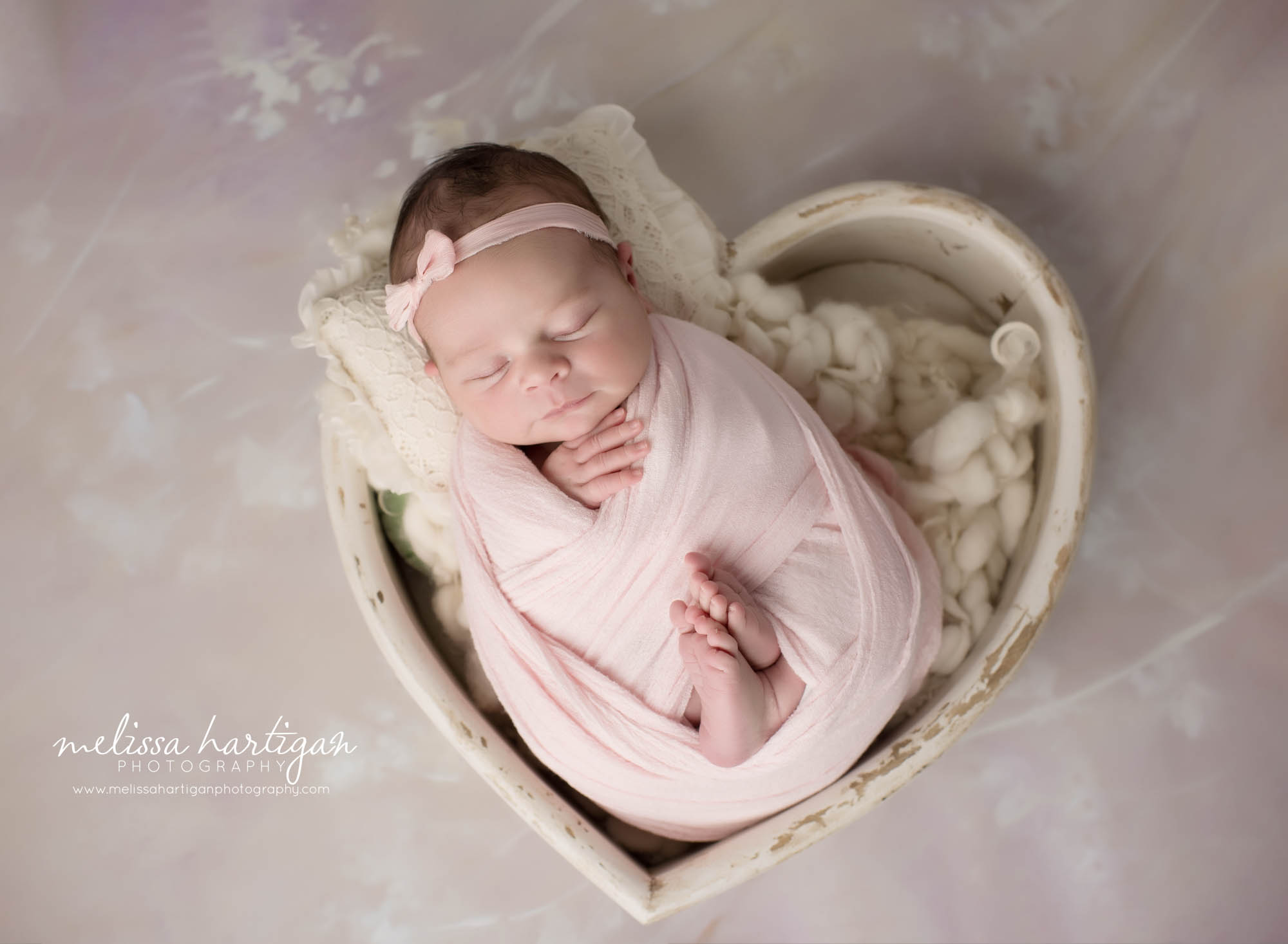 newborn baby girl wrapped in pink wrap posed in wooden heart prop with pink bow headband hartford county newborn photography