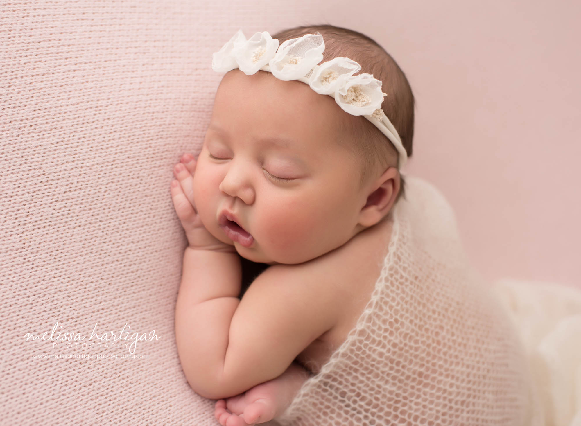 newborn baby girl posed on pink backdrop with knitted drapping layer