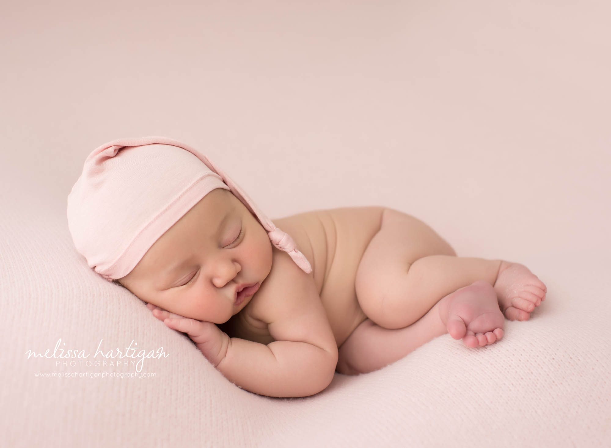 newborn baby girl posed on side tummy wearing pink sleepy cap new london county ct baby photography