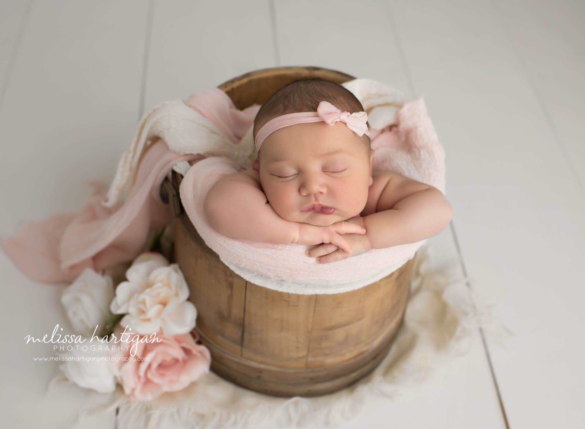 newborn baby girl posed in wooden barrel with cream and pink flowers wearing pink bow headband new london county CT newborn photography
