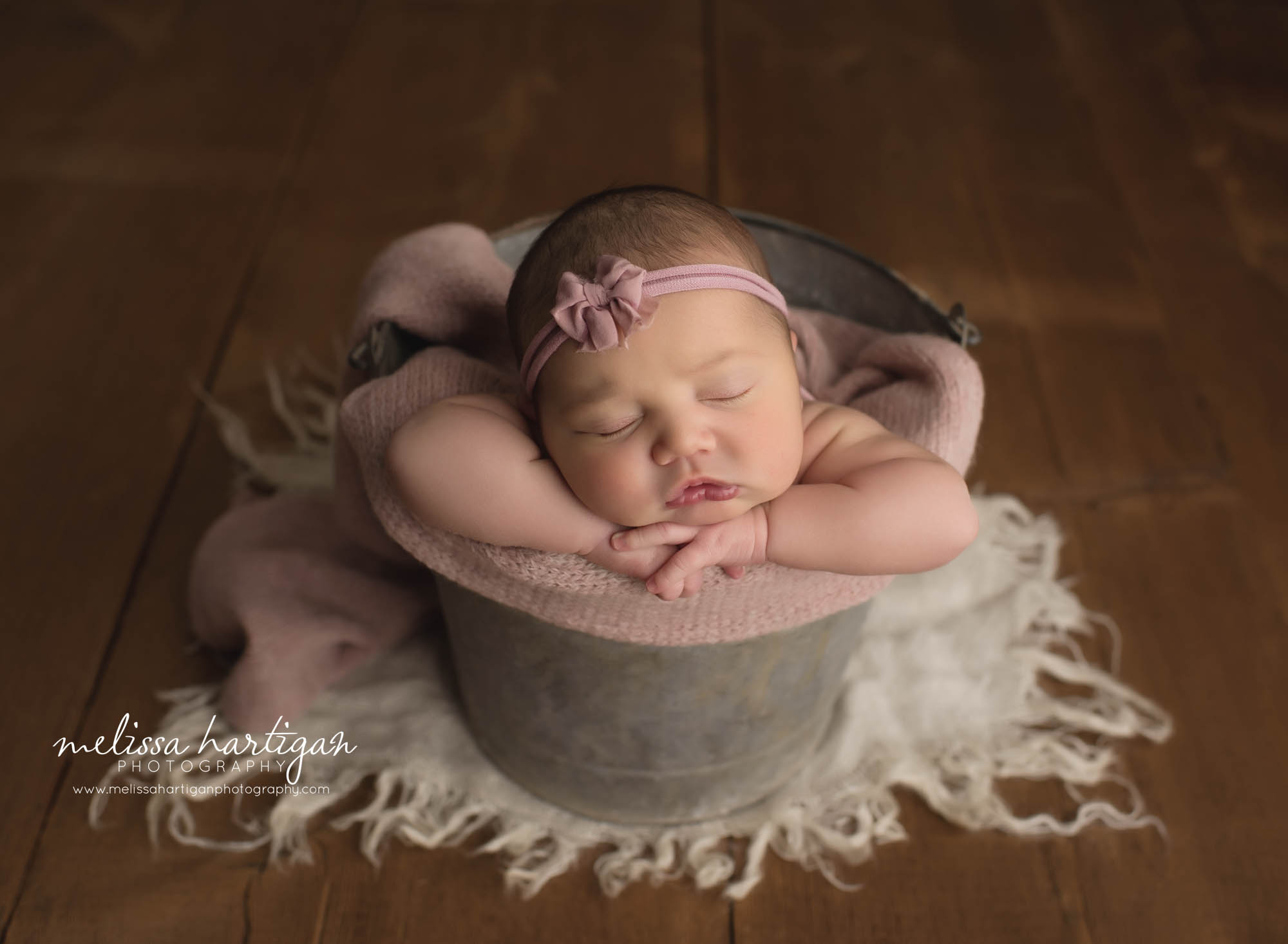 newborn baby girl posed in metal bucket with pink bow headband and pink layer new london county newborn photography