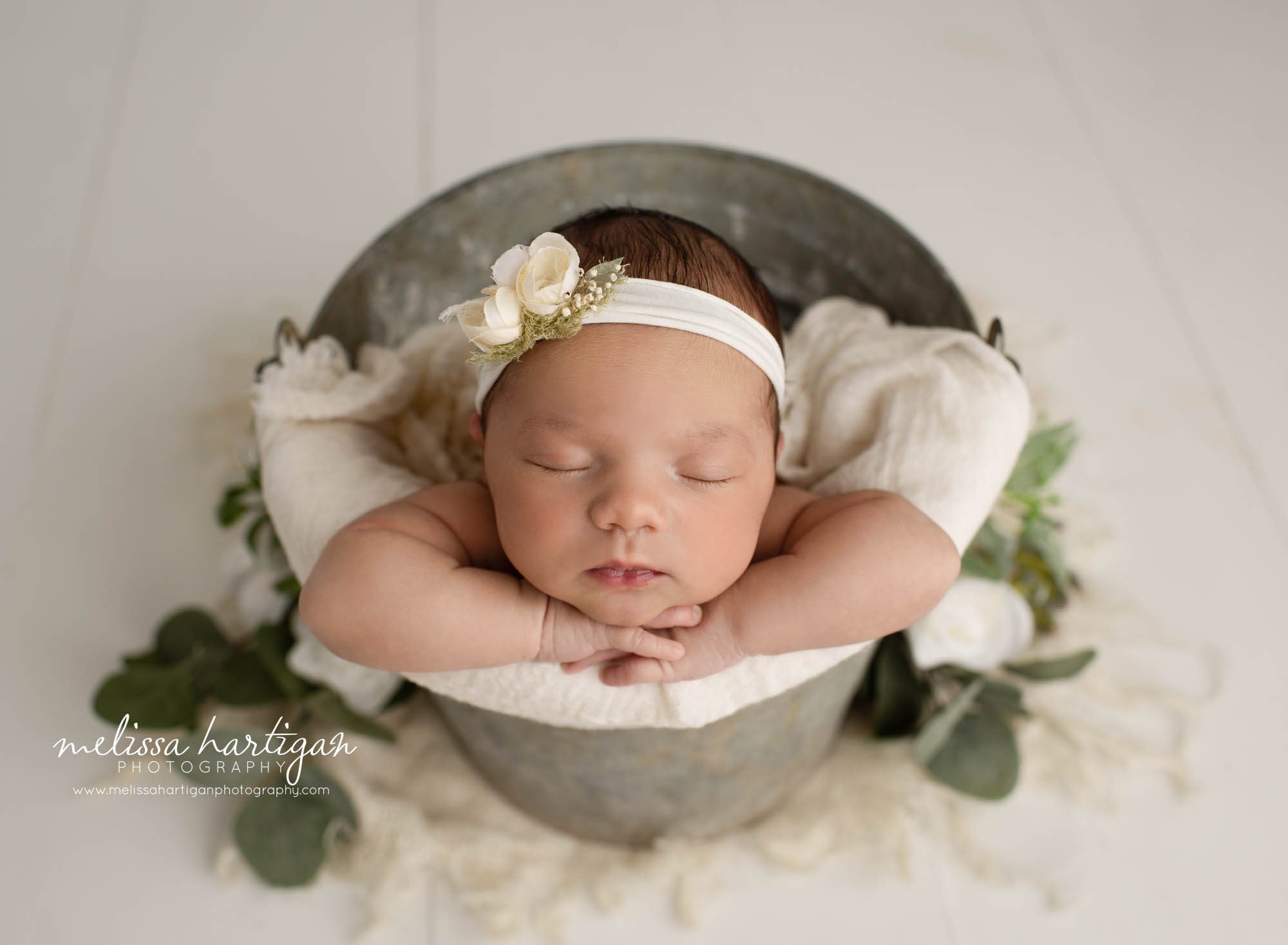 newborn baby girl posed in metal bucket wearing cream floral headband