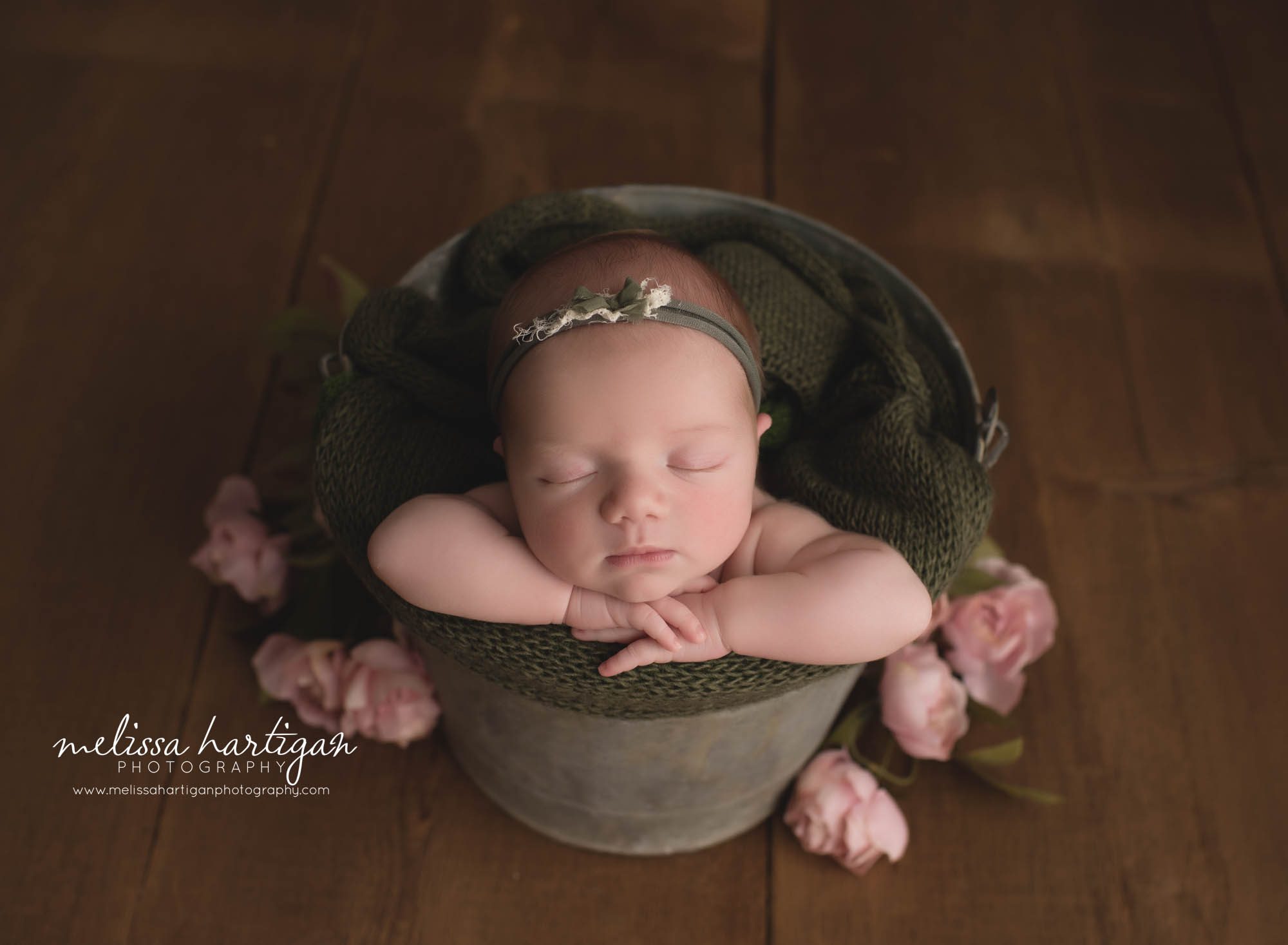 newborn baby girl posed in metal bucket with green knitted layer wrap and pink flowers tolland county newborn photography
