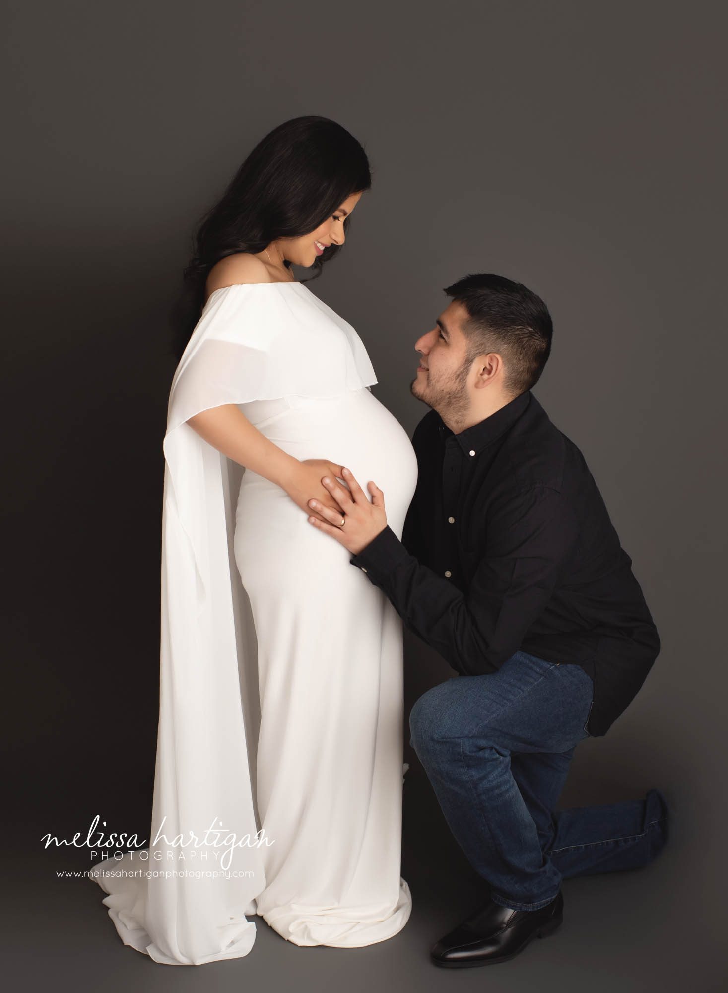 couple in studio maternity photography pose dad kneeling holding side of belly