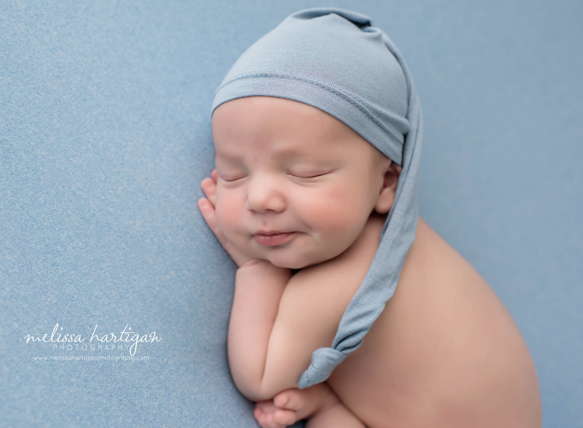 newborn baby boy posed on tummy wearing blue colored sleepy cap CT newborn photography