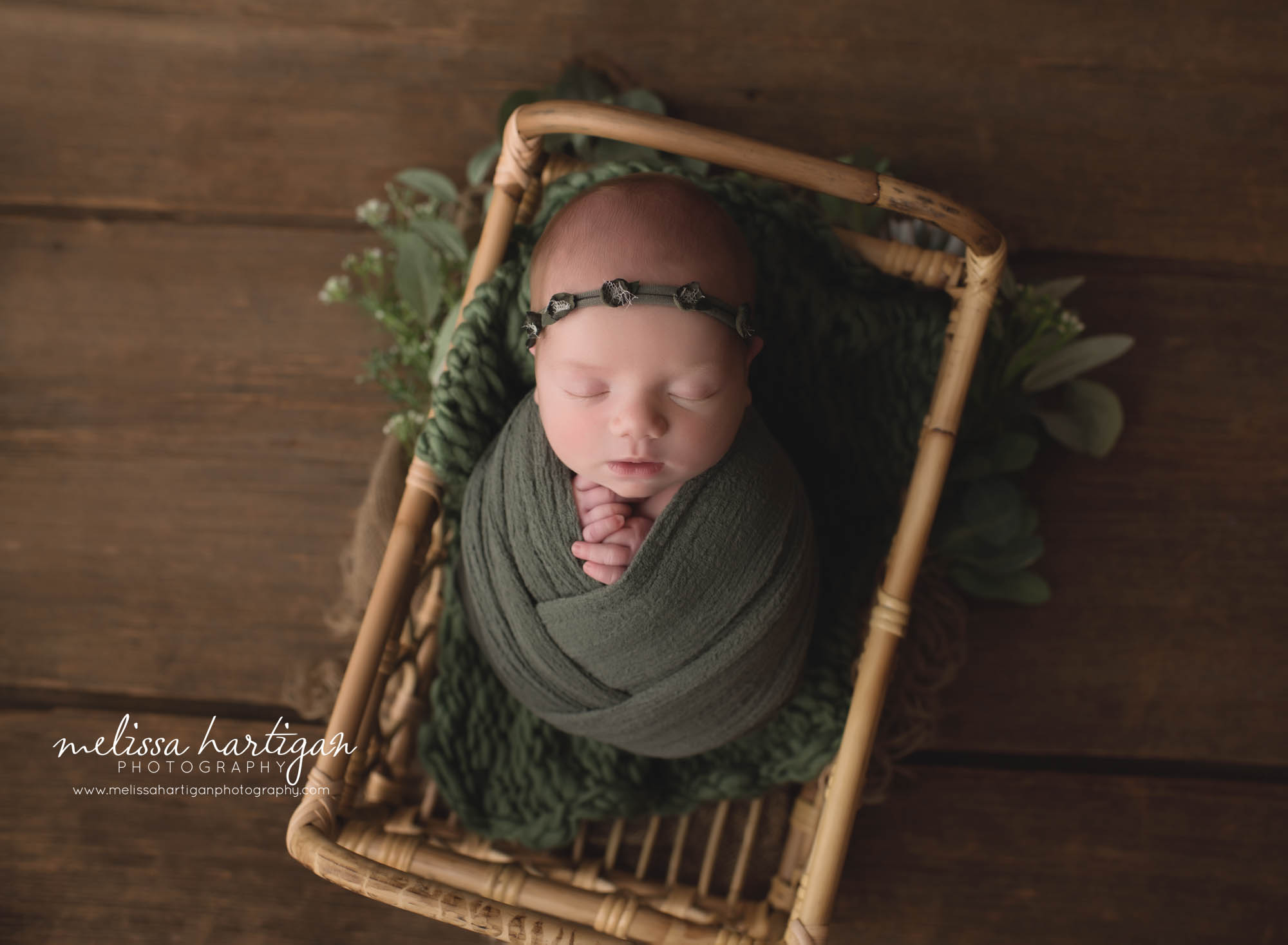 newborn baby girl wrapped in green wrap posed in basket with green headband