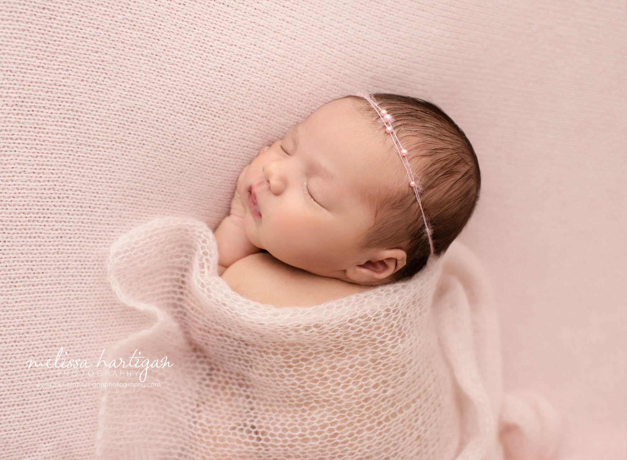 newborn baby girl sleeping pn tummy with hand under chin with pink knitted layer draped over east hartford baby photography