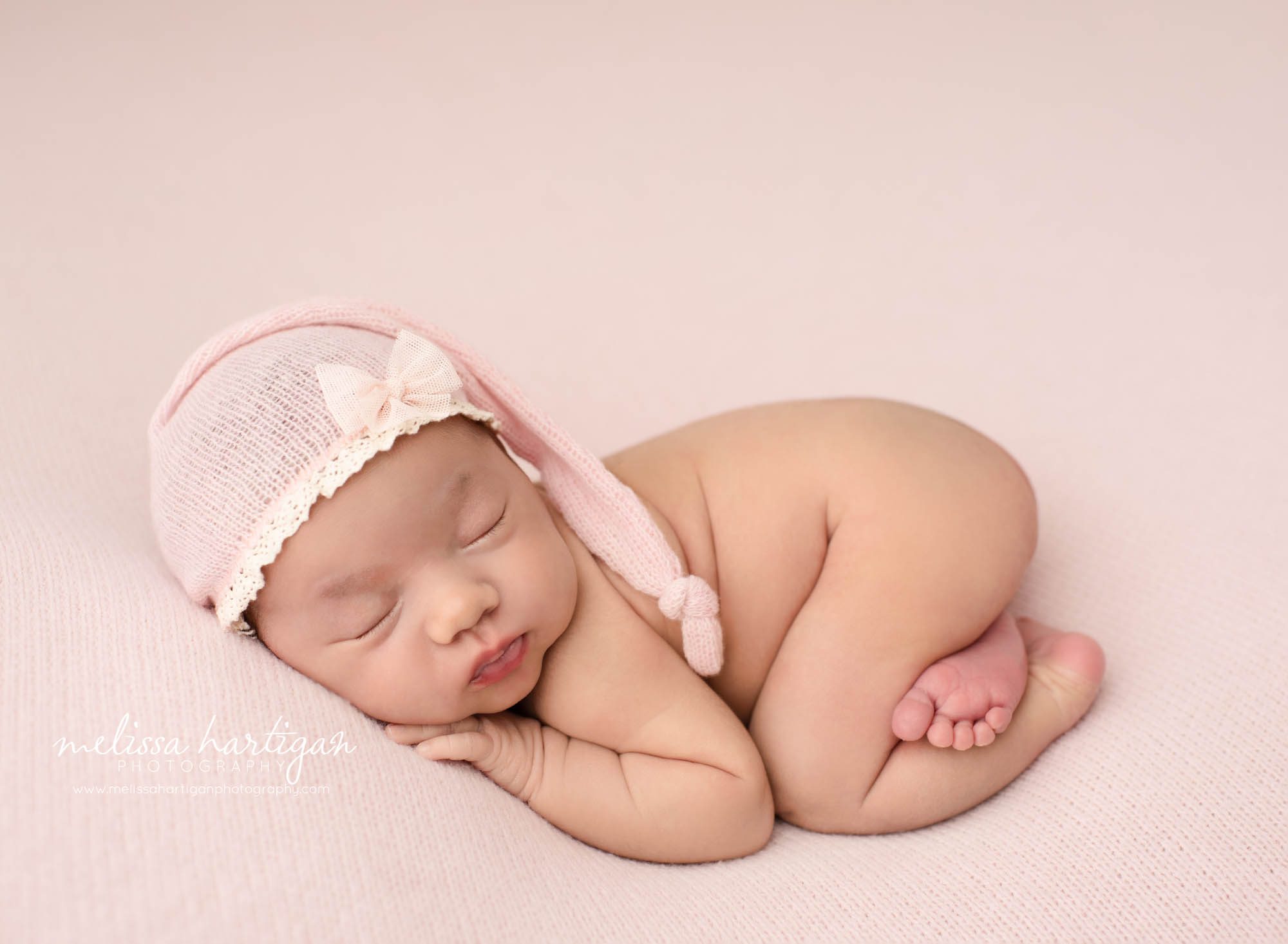 newborn baby girl posed on tummy bump up wearing pink knit sleepy cap with lace detail and bow east hartford newborn photography