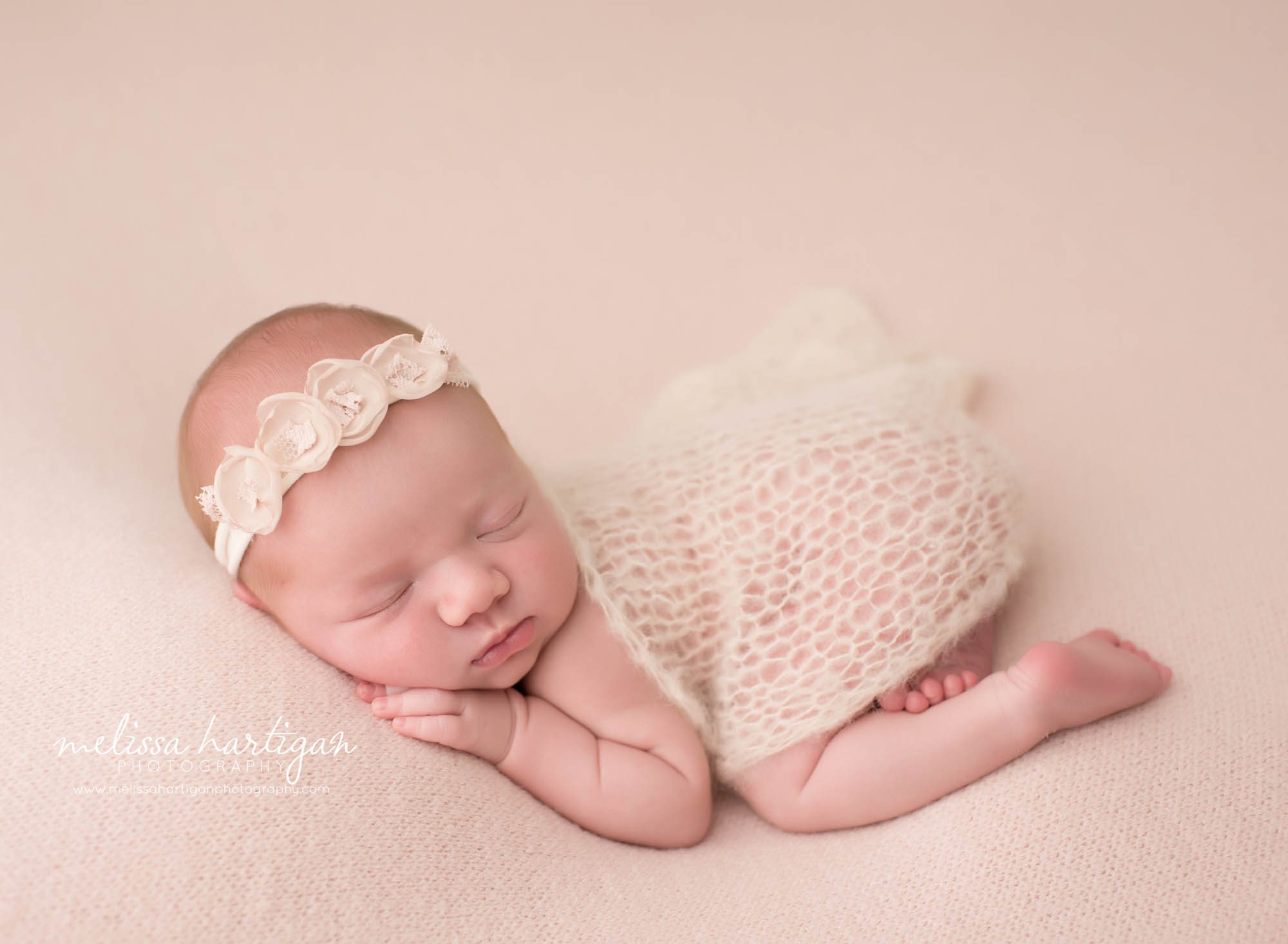 newborn baby girl posed on tummy wearing floral headband with delicate knitted lace wrap draped over her