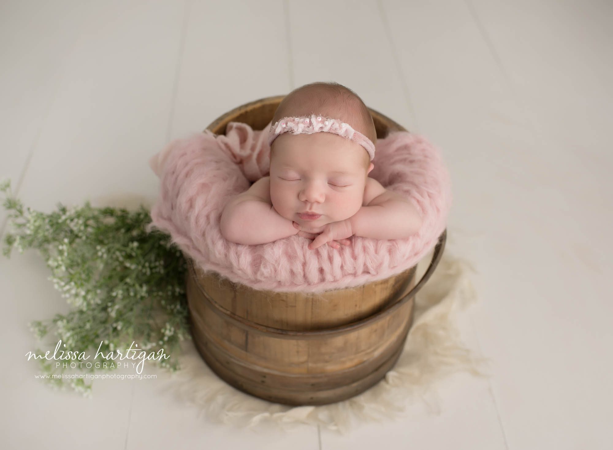 newborn baby girl posed in wooden barrel with knitted pink layer