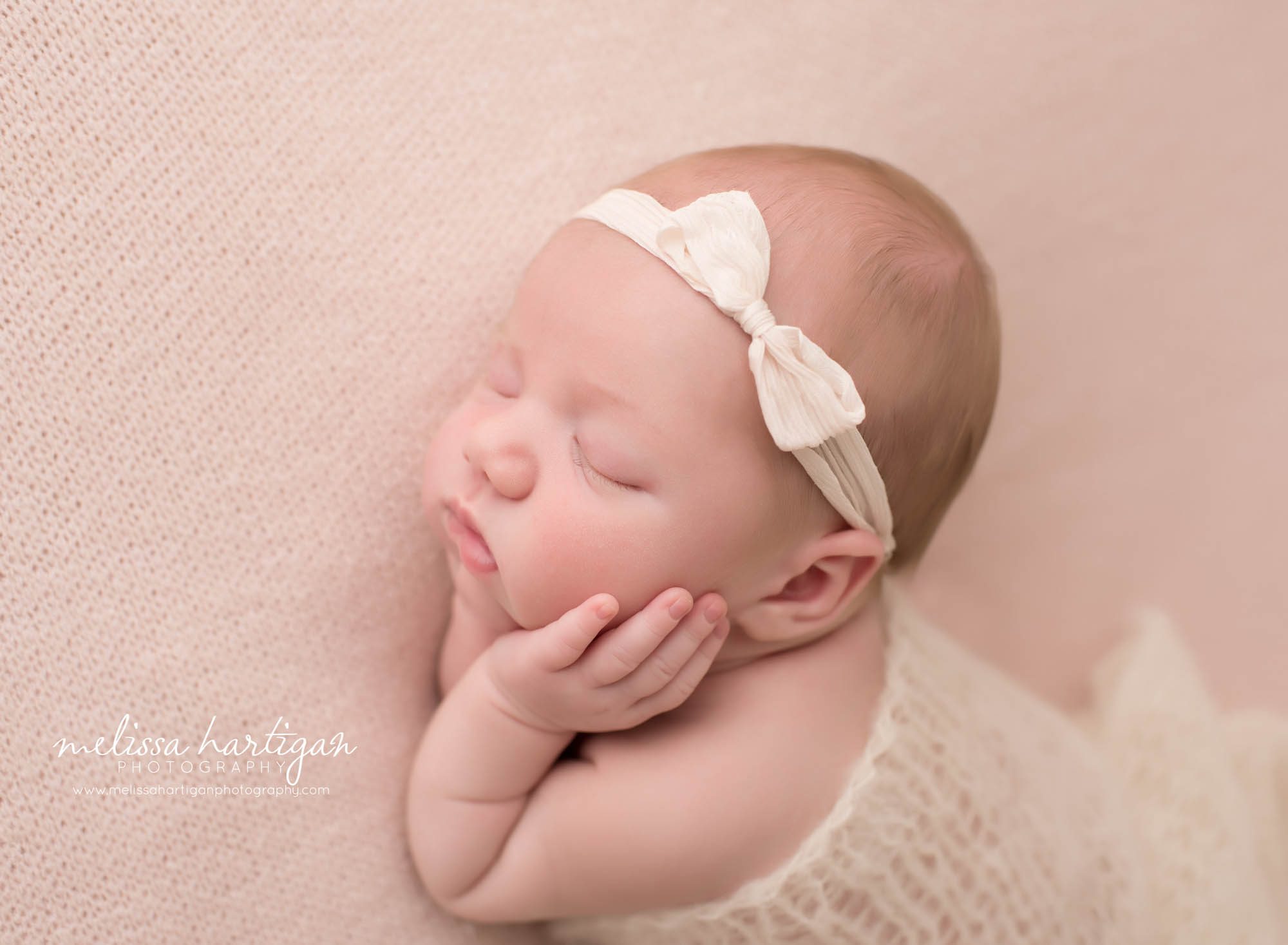 newborn baby girl posed with hands under cheeks laying on her side wearing cream bow headband