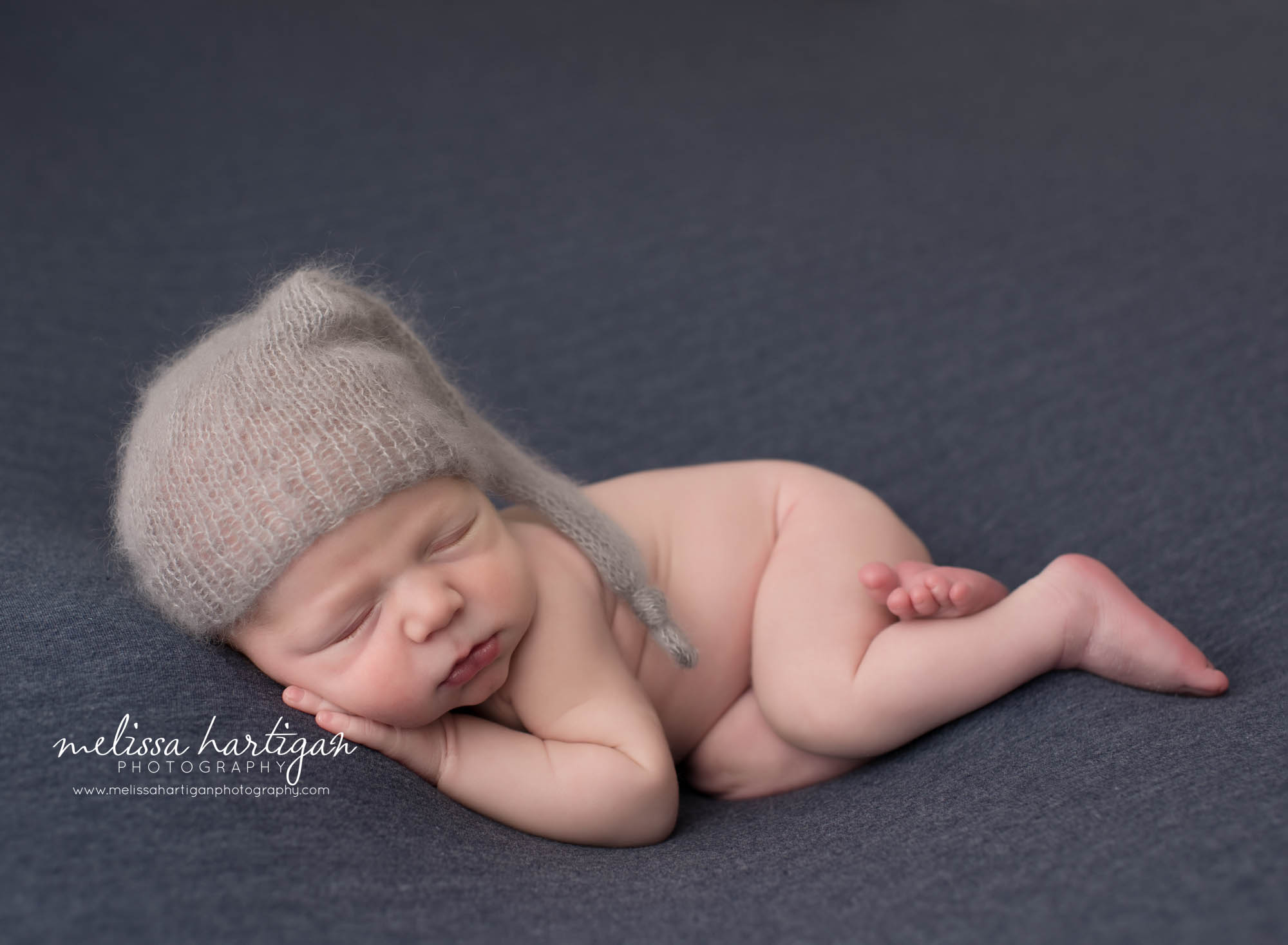 newborn baby boy posed on tummy with hand under cheek wearing gray sleepy cap