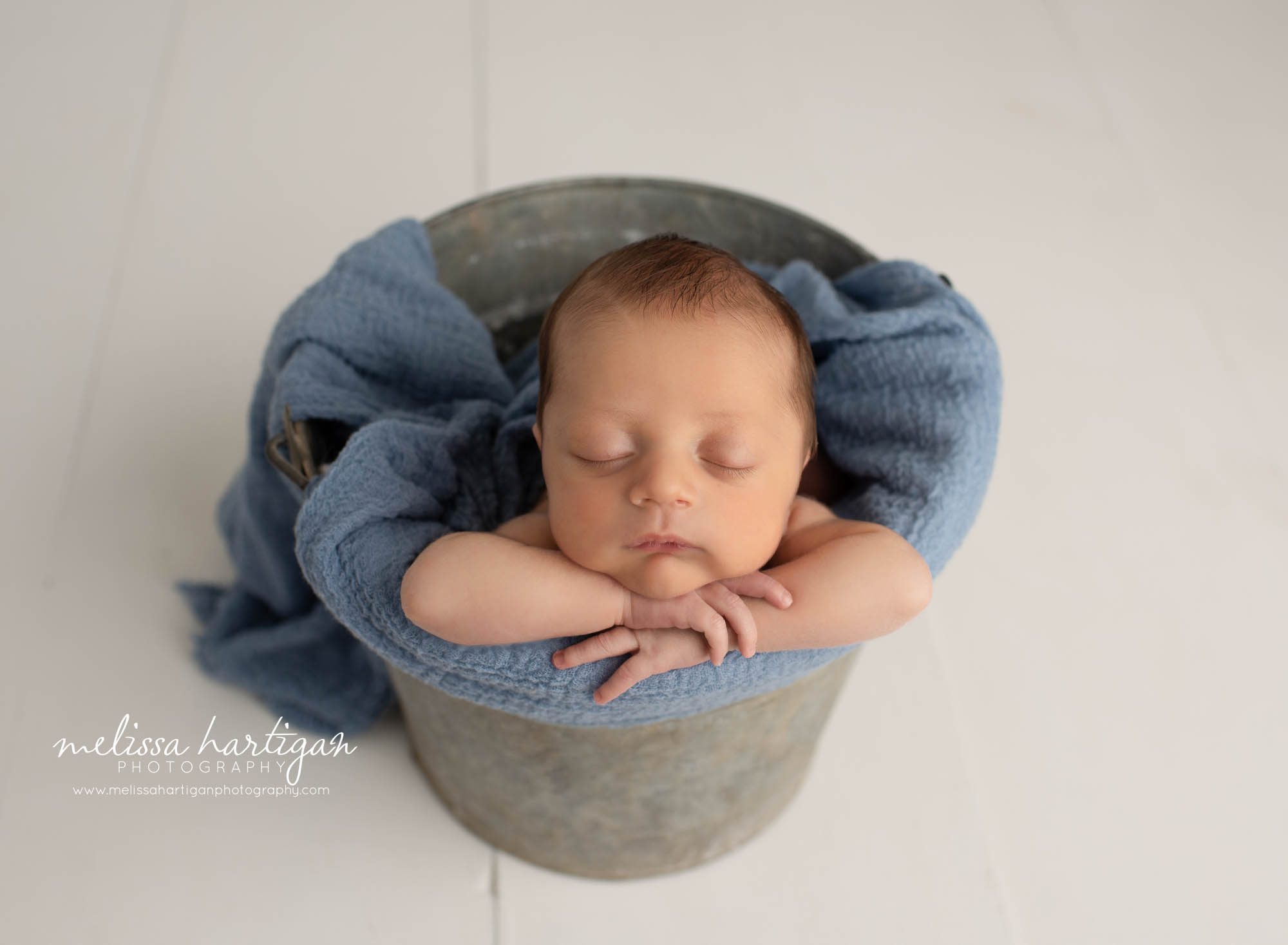 Baby boy posed in bucket with blue wrap draped CT newborn photographer