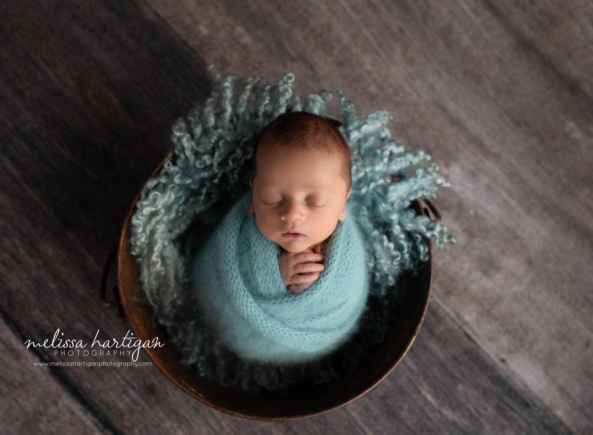 newborn baby boy posed in bucket with teal blue curly layer wrapped in knitted wrap