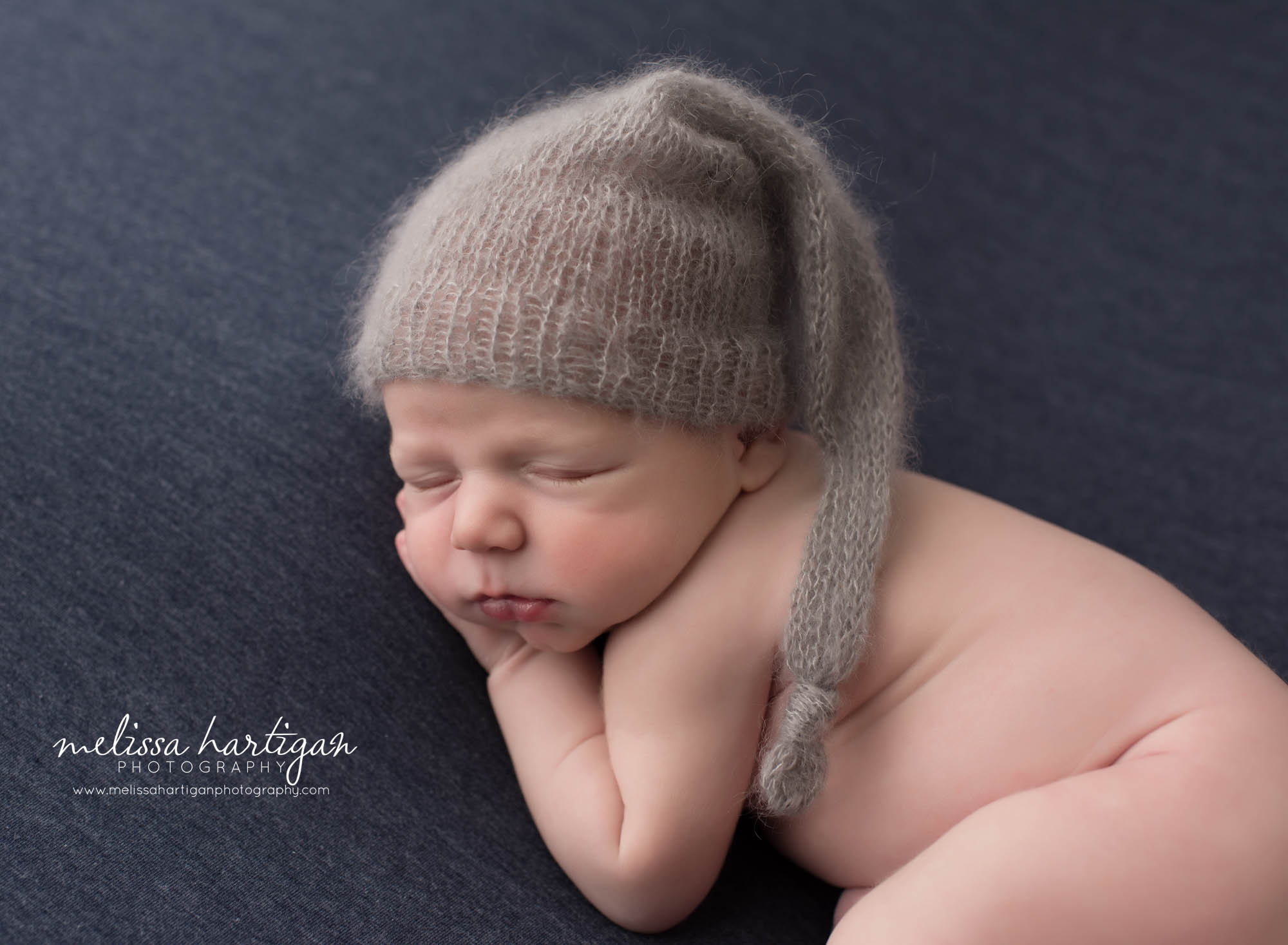 newborn baby boy posed on blue backdrop with gray knitted sleepy cap