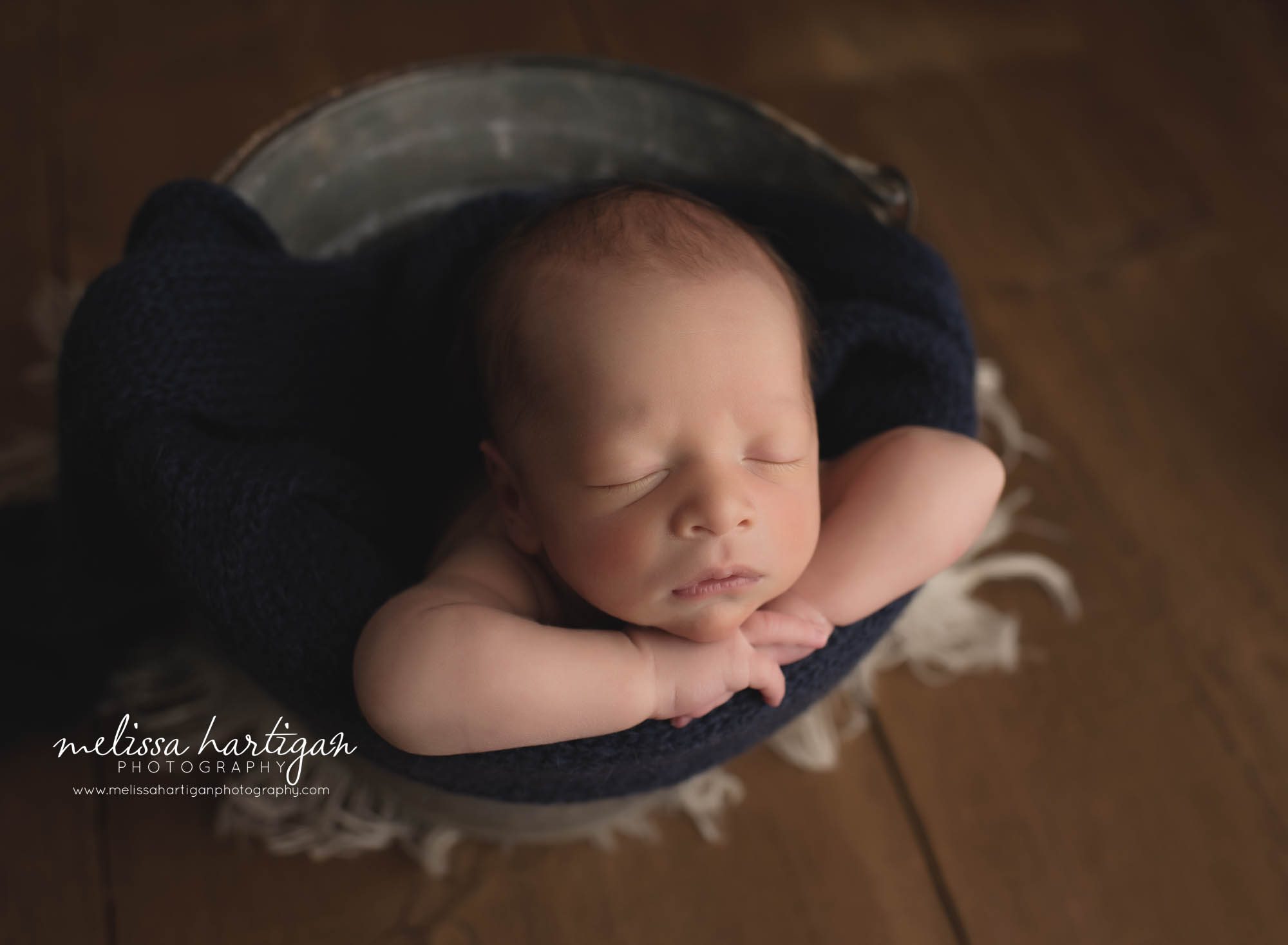newborn baby boy posed in bucket withnavy blue knitted wrap
