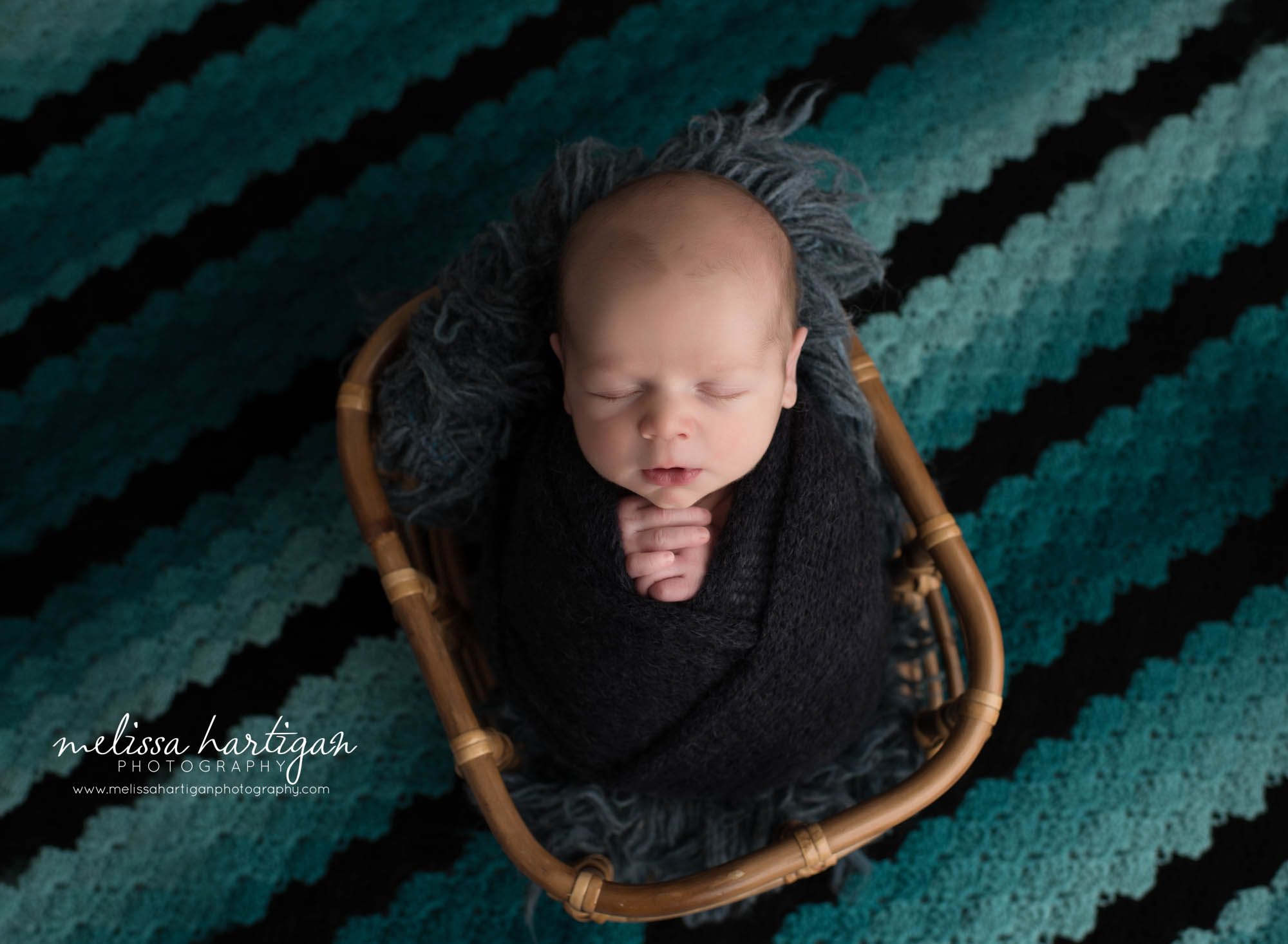 newborn baby boy wrapped in navy blue posed in basket with teal and black knitted baby blanket