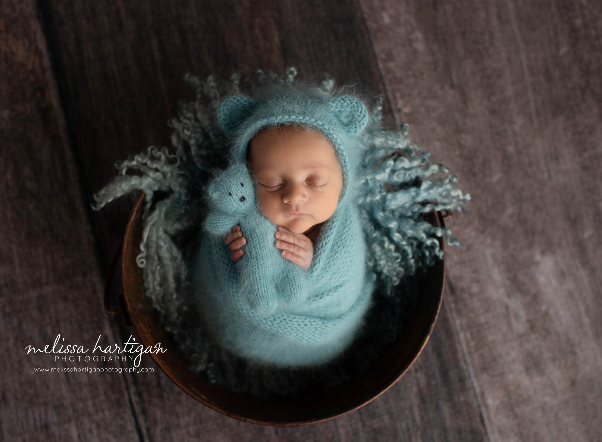 newborn baby boy wrapped in teal blue knitted wrap with matching bear bonnet and teddy bear