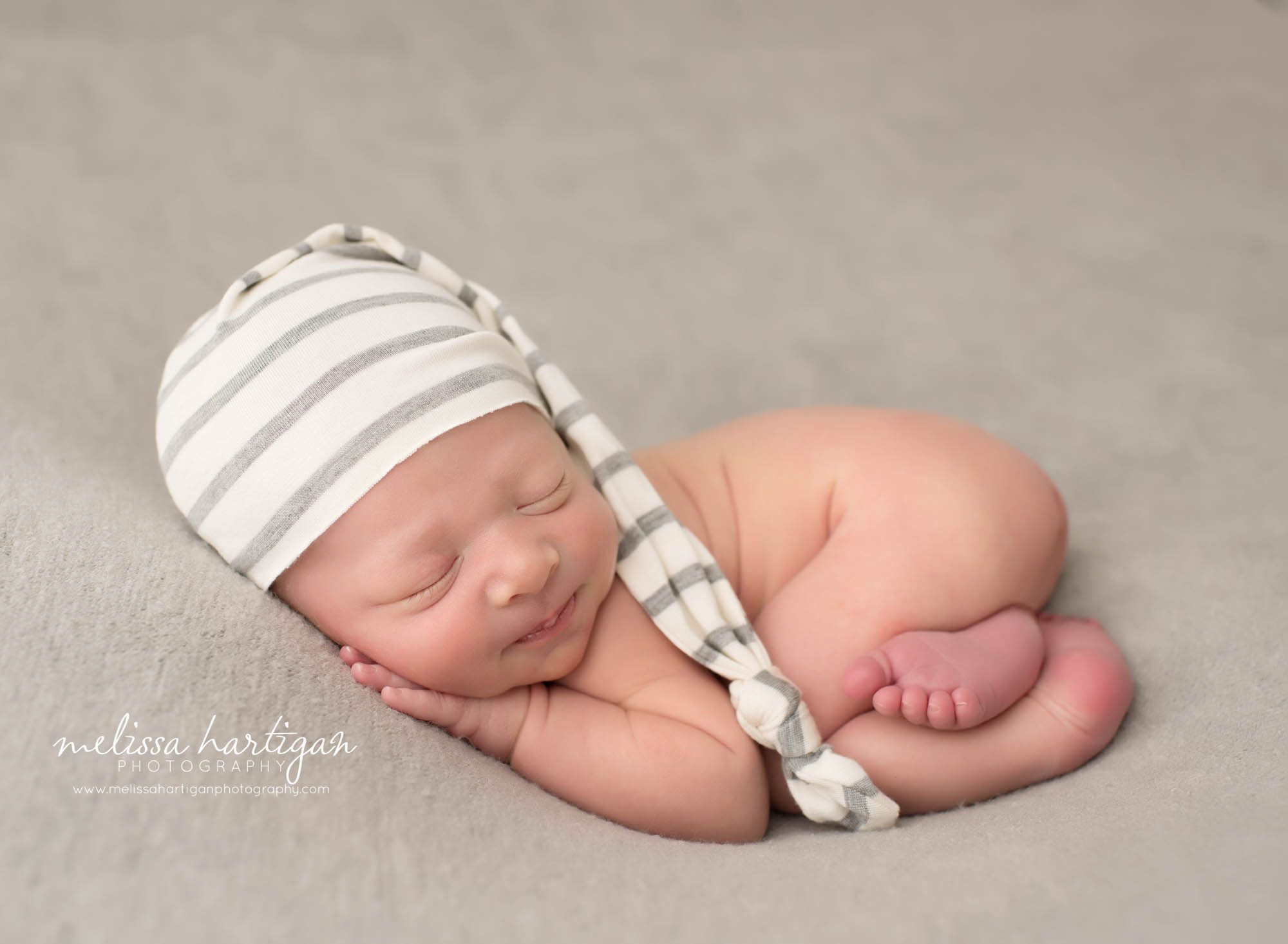 newborn baby boy posed on tummy wearing cream and gray striped long sleepy cap middletown newborn photography