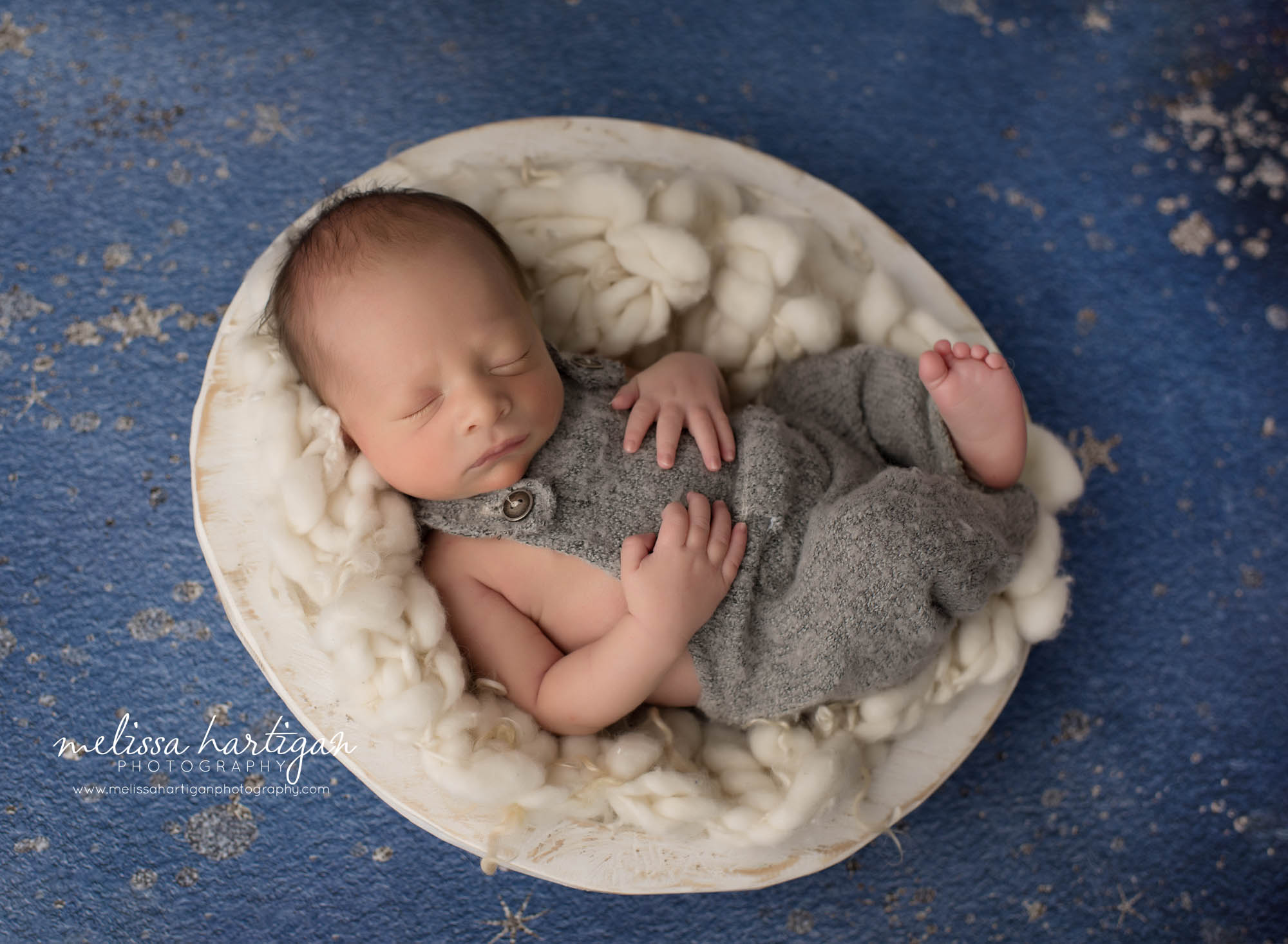 newborn baby boy posed in cream bowl with cream colored fluff wearing gray newborn boy outfit