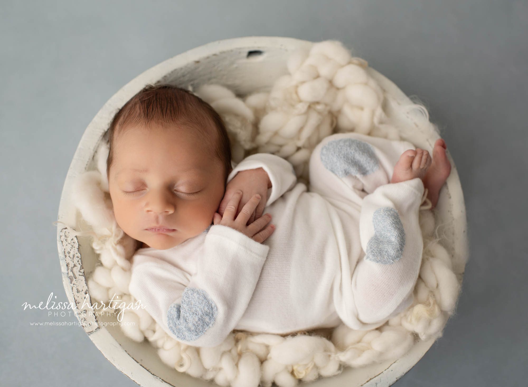 newborn baby boy posed cream bowl wearing cream colored outfit with blue patches on it