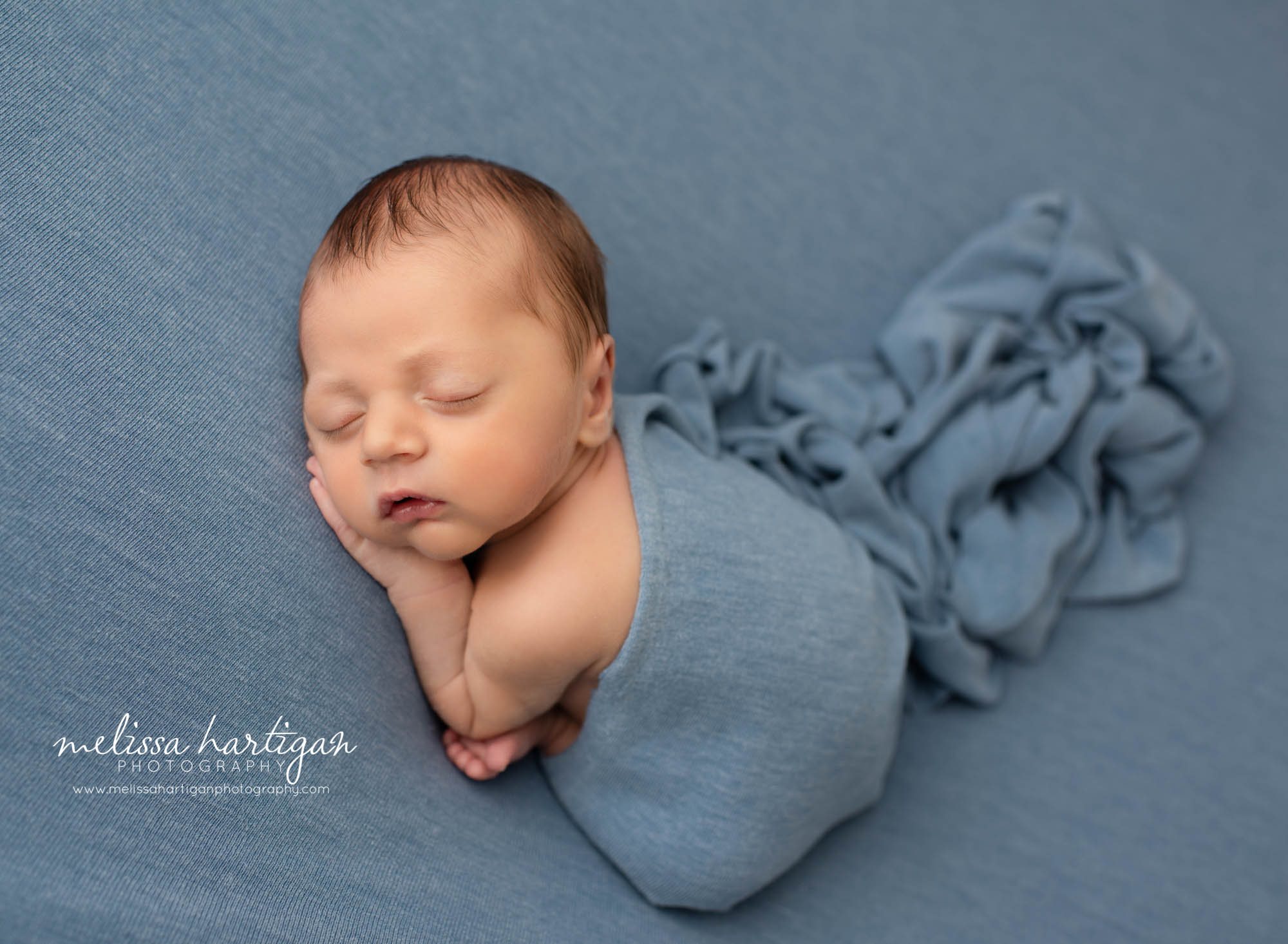 newborn baby boy posed on blue backdrop with wrap draped over newborn photographer CT