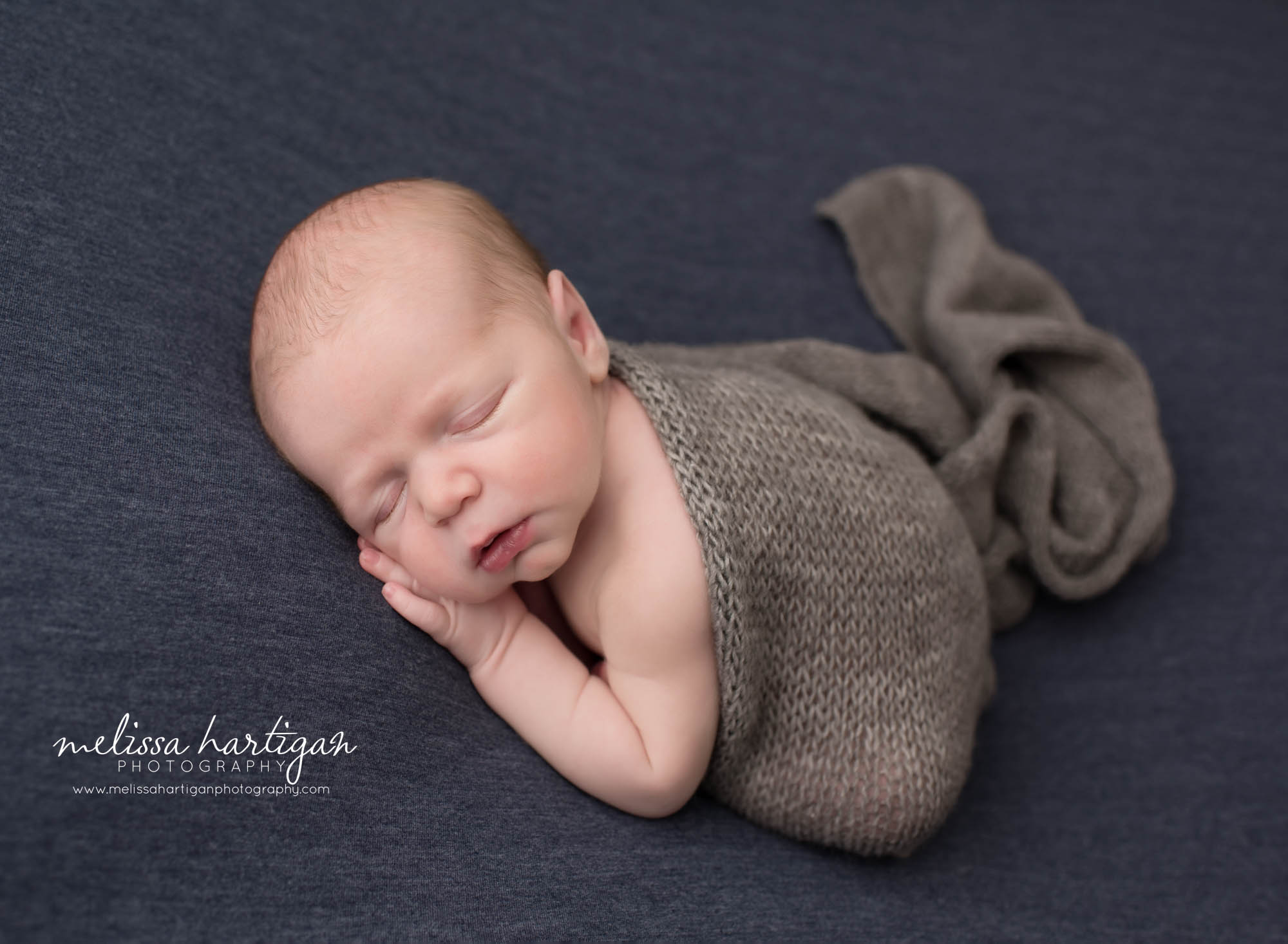 newborn baby boy posed on blue backdrop with gray knitted wrap Newborn Photography Middlesex county CT