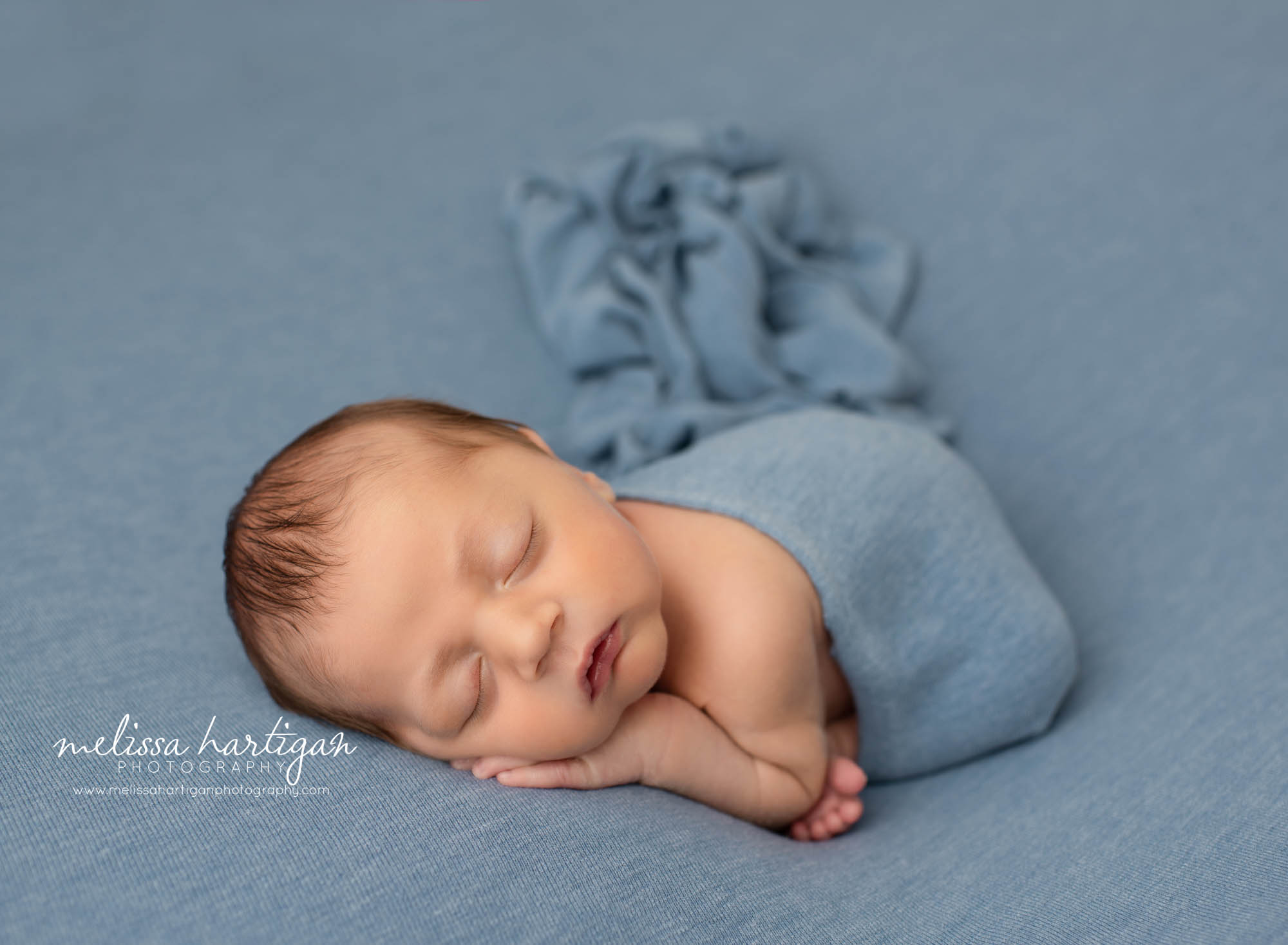 newborn baby boy posed on tummy taco pose with wrap draped over