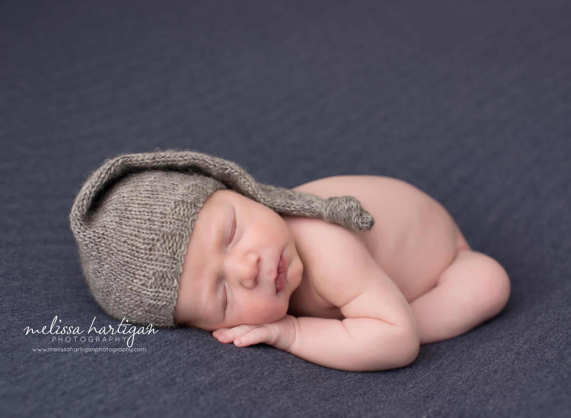 newborn baby boy posed on tummy wearing gray knitted sleepy cap